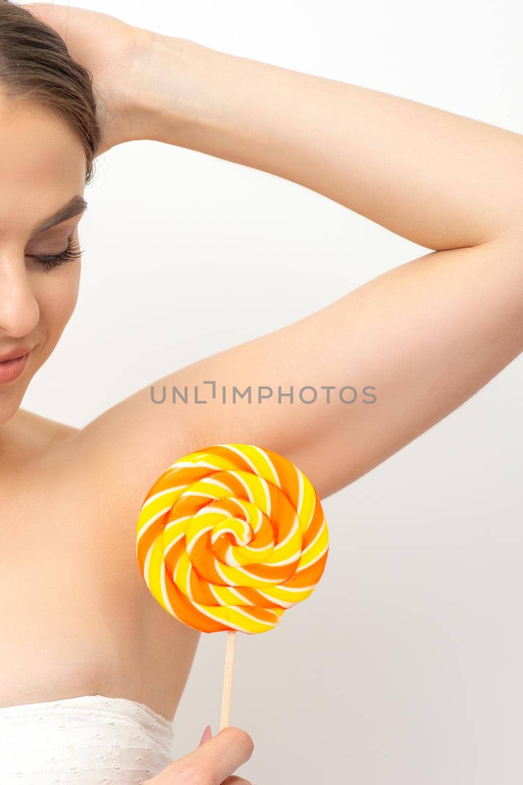 Waxing, depilation concept. The beautiful young caucasian woman covers her armpit with a lollipop on white background. by okskukuruza