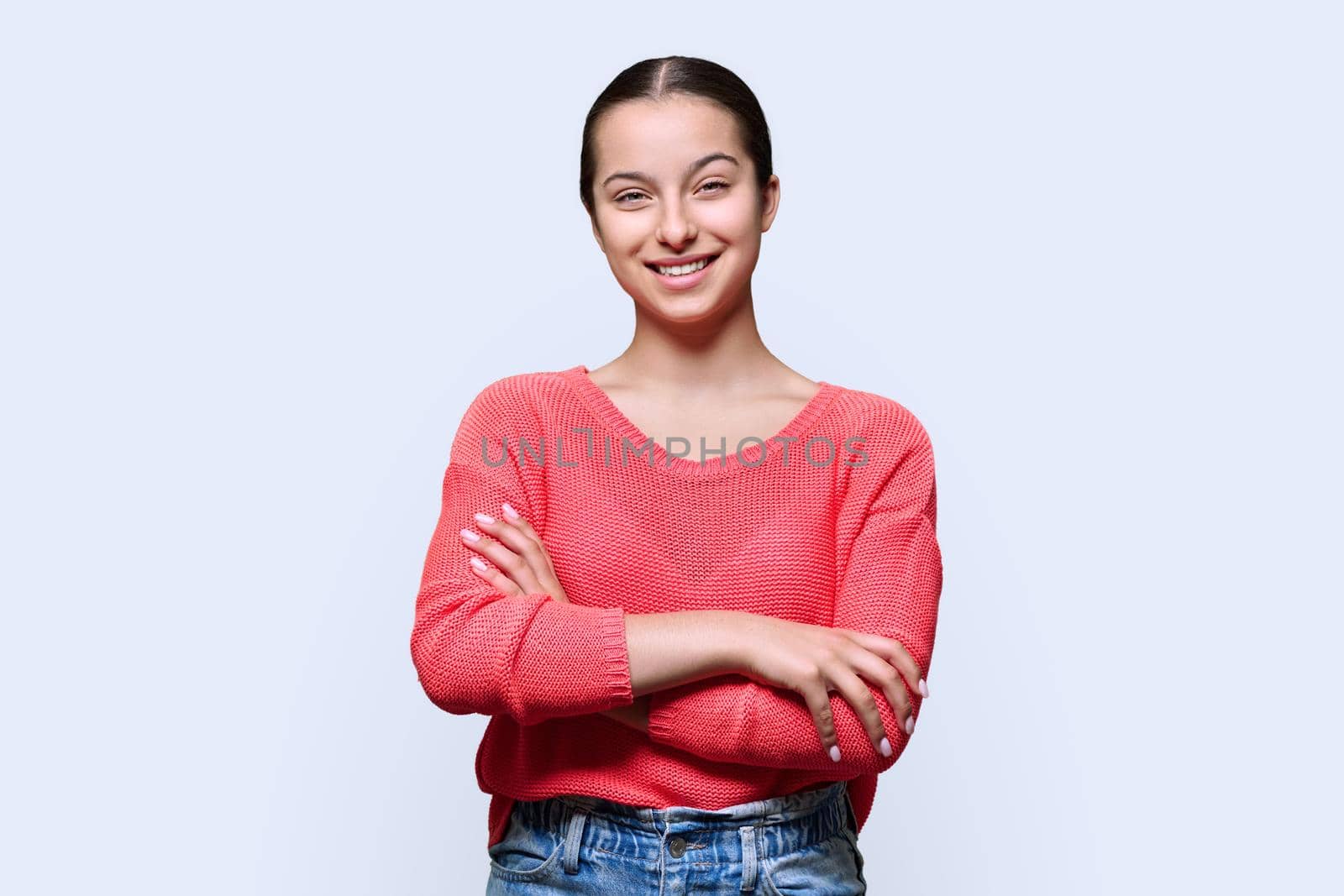 Portrait of teenage smiling female looking at camera on light studio background. Confident teen girl with crossed arms in red. Adolescence, high school, youth 15, 16 years old concept