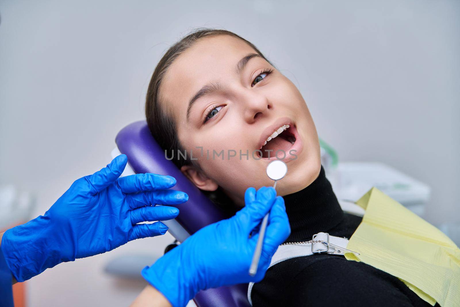 Young teenage female at dental checkup in clinic. Teenage girl sitting in chair, doctor dentist with tools examining patient's teeth. Adolescence, hygiene, dentistry, treatment, dental health care