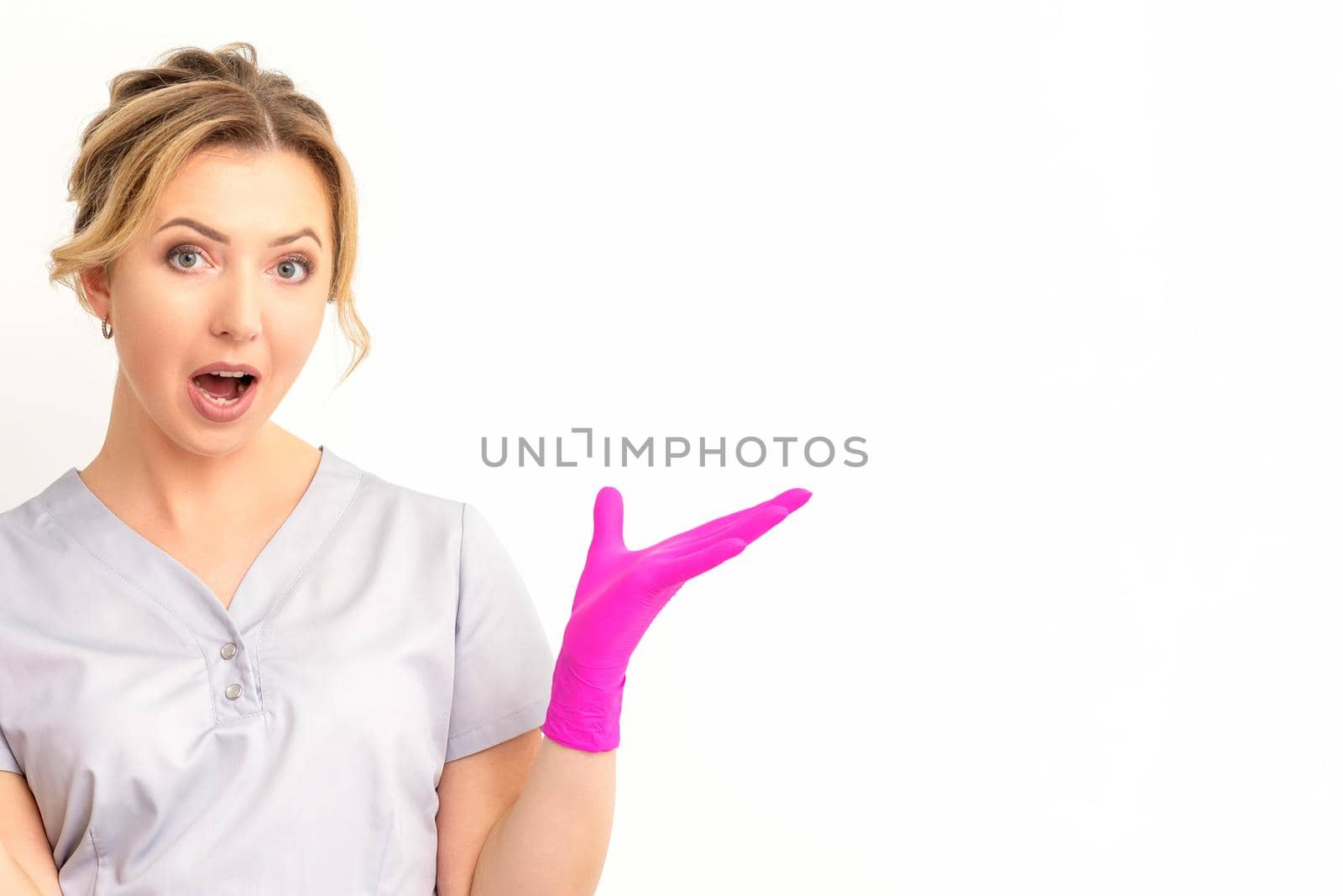 Body language. Young surprised Caucasian woman doctor wearing gloves gesturing with her hands, spread his arms having shocked expression opening her mouth against the white background