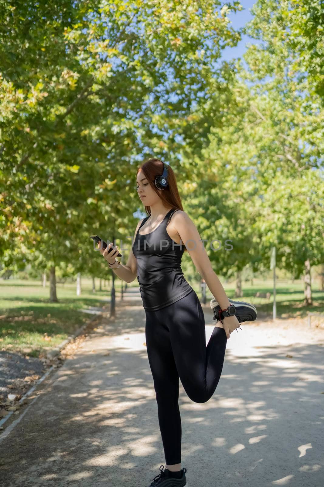 Portrait of fit and sporty young woman doing stretching in public park. by barcielaphoto