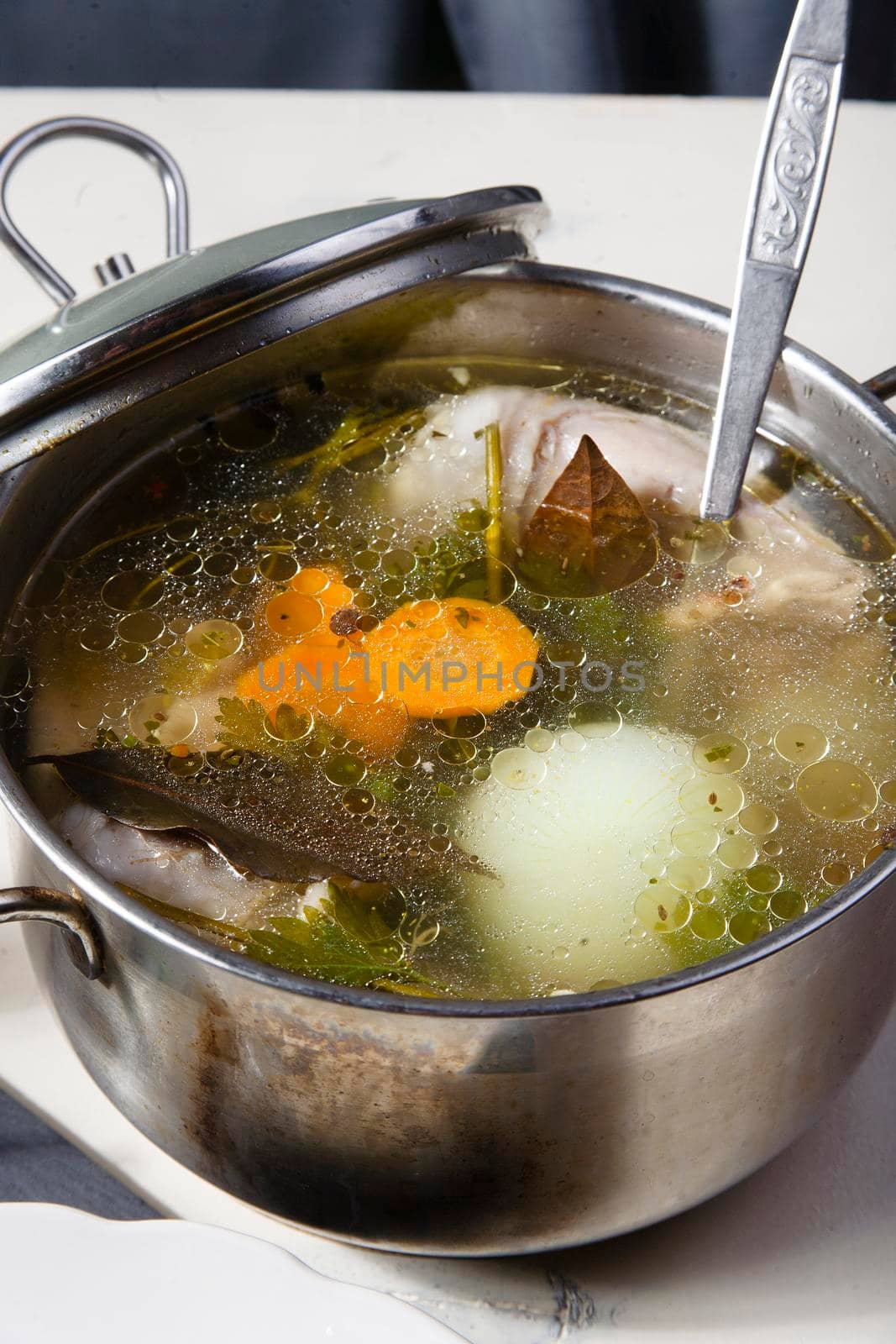 Freshly home made chiken broth in kitchen pan with ladle on white table, home made simple lanch concept, close up, selective focus.