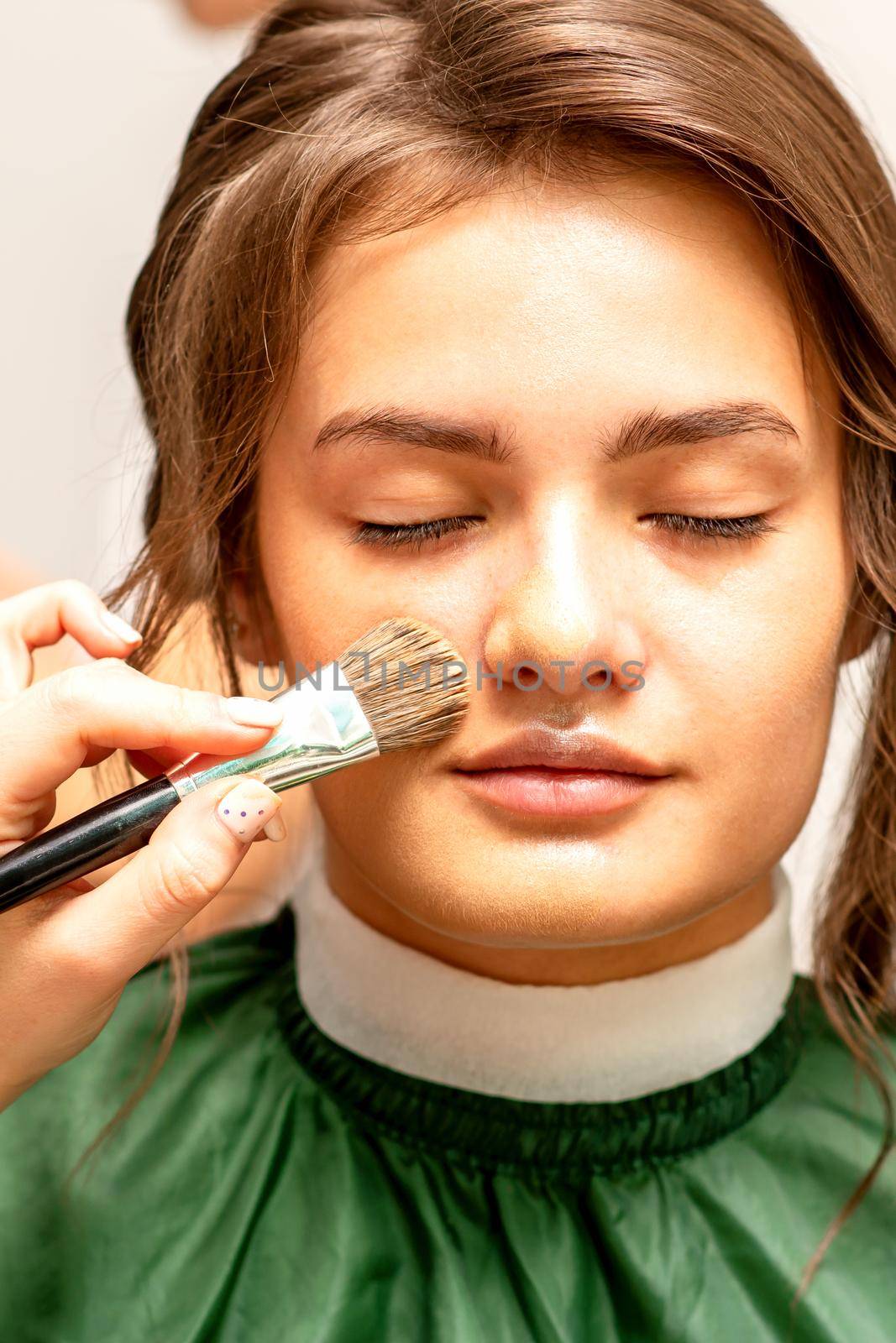 The makeup artist applies a cosmetic tonal foundation on the face using a makeup brush