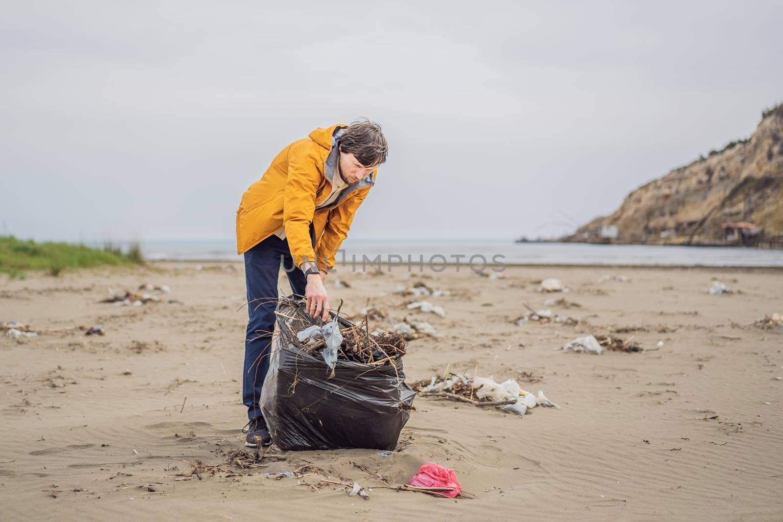 Plastic garbage. Sea and ocean pollution. Beach clean up. Young man picking used plastic bottles on sand shore. Environmental activist collecting rubbish. Save our Earth. Nature protection.