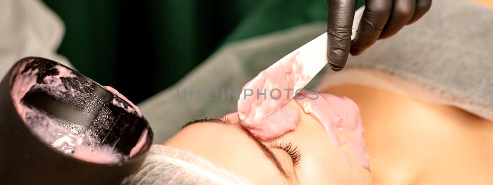 Beautiful young caucasian woman receiving an alginic mask to the face in beauty salon. Facial skin treatment. by okskukuruza