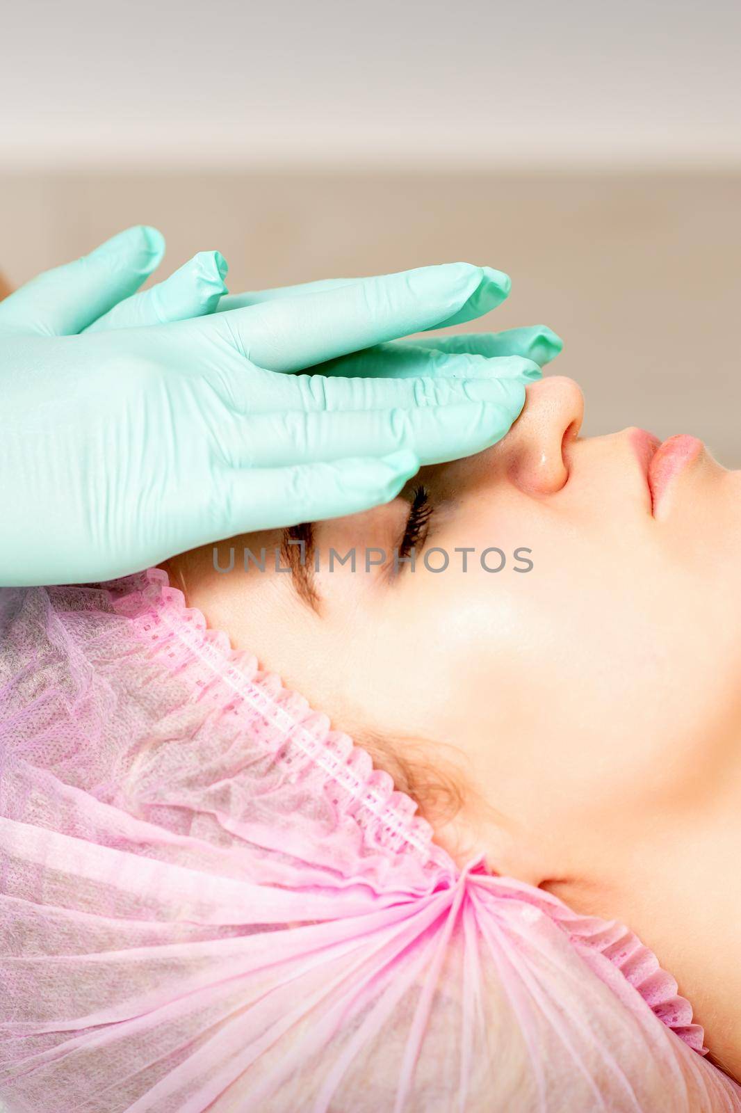 Cosmetologist with gloved hands applies a moisturizing mask with peeling cream on the female face. Facial cosmetology treatment. Procedures for facial care