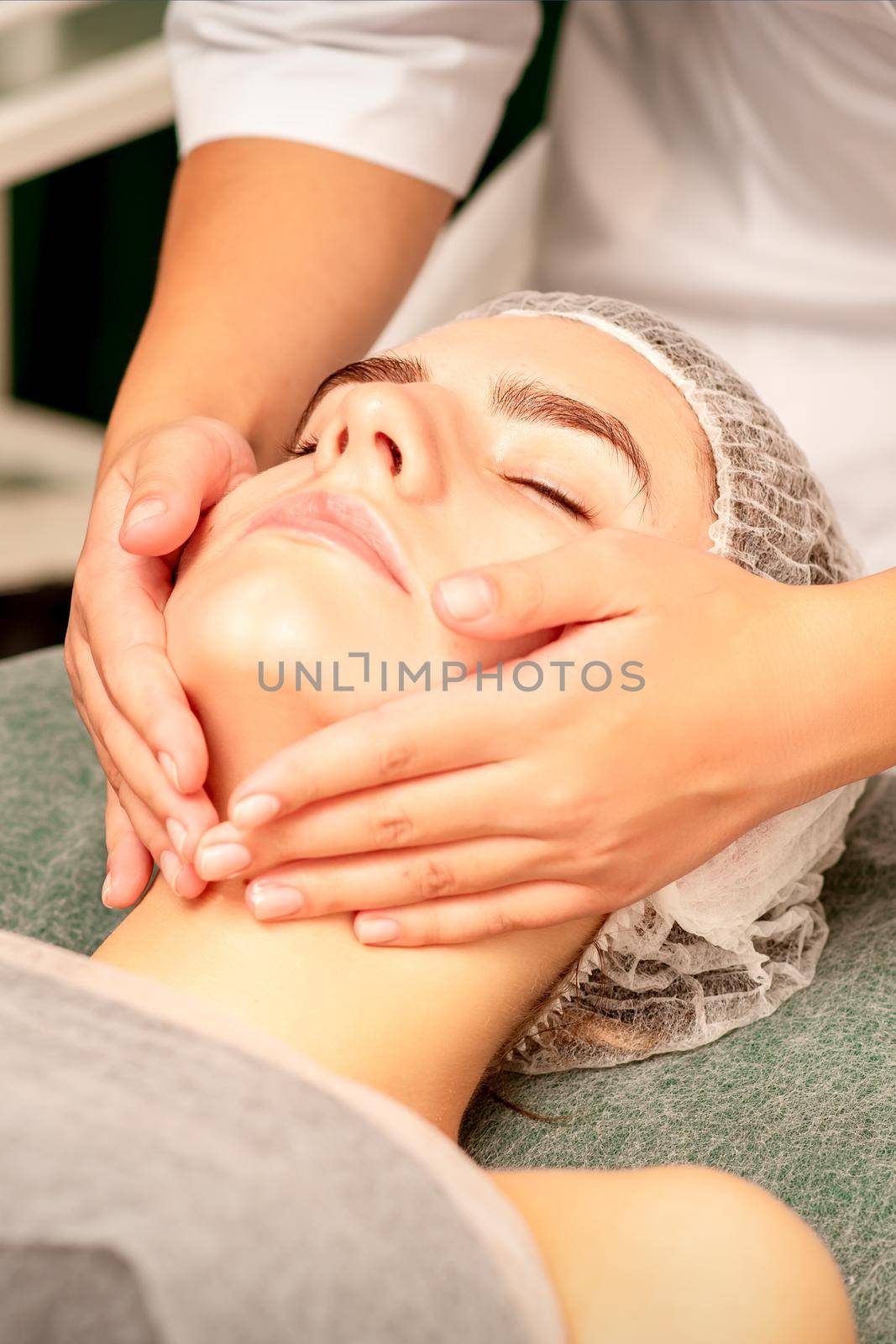 Facial treatment massage. Beautiful young caucasian woman with perfect skin receiving face and neck massage at a beauty spa