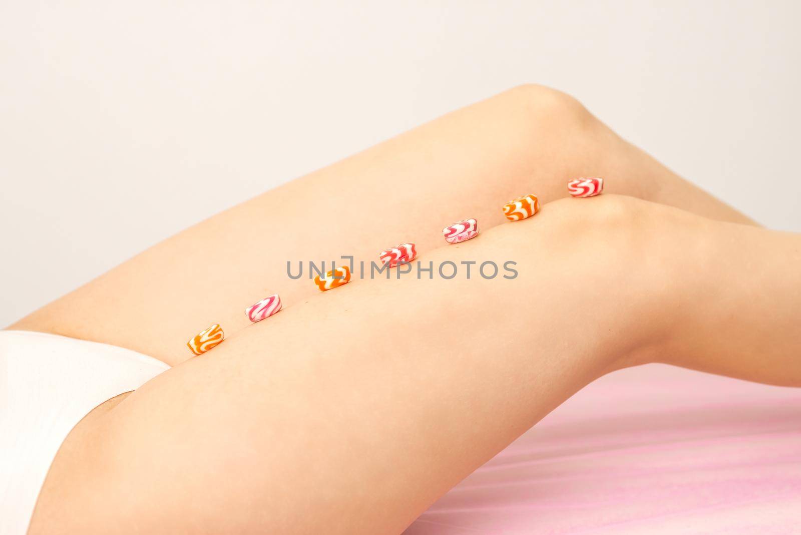 Depilation, waxing concept. Round candies lying down in a row on the female leg, close up. by okskukuruza