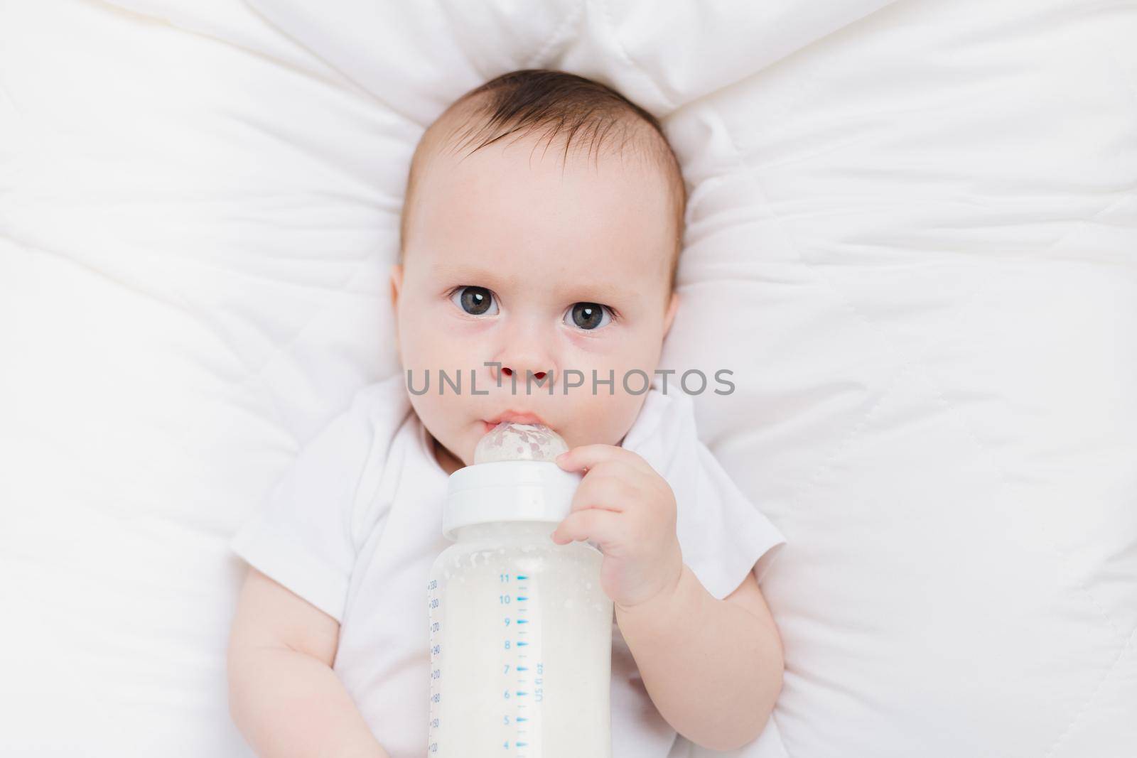 The baby in his crib eats from a bottle . Baby food copyspace . Artificial feeding. Kid top view