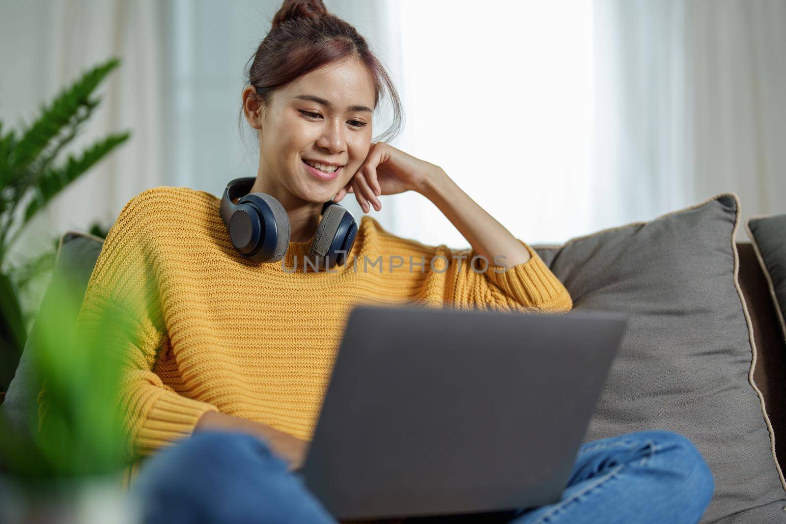 Portrait of a young Asian woman using a computer on the sofa by Manastrong