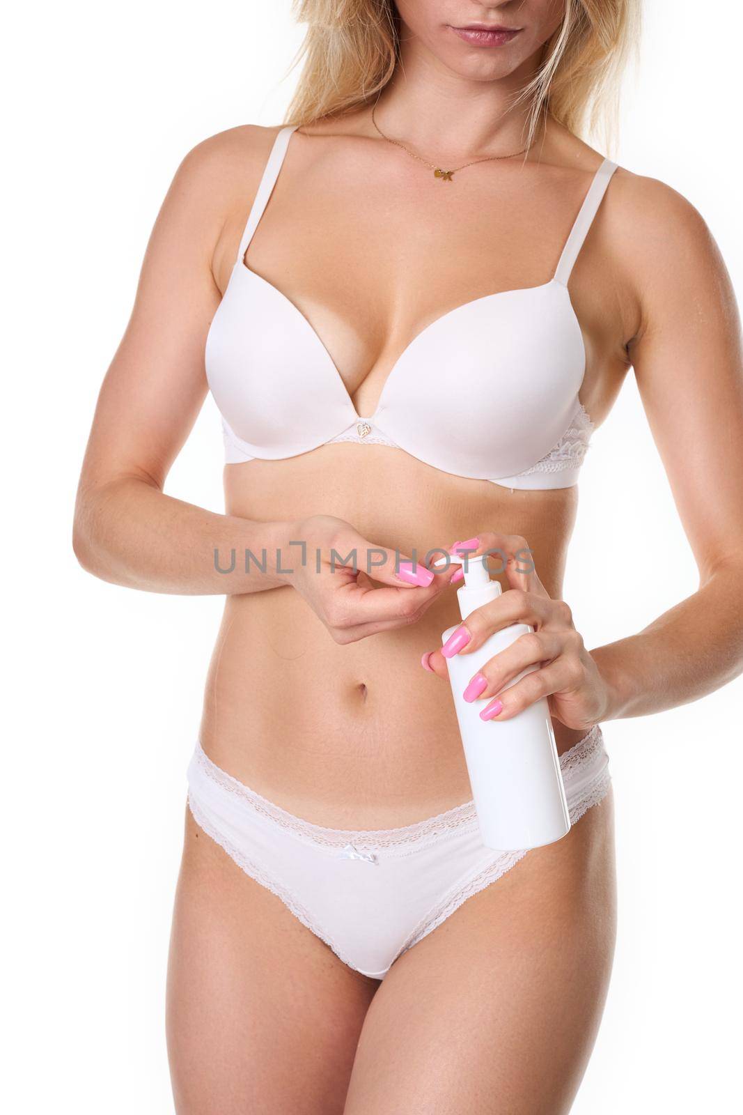 a woman with blonde hair poses in white lingerie and uses a body lotion. Photo taken in the studio. photo on a white background