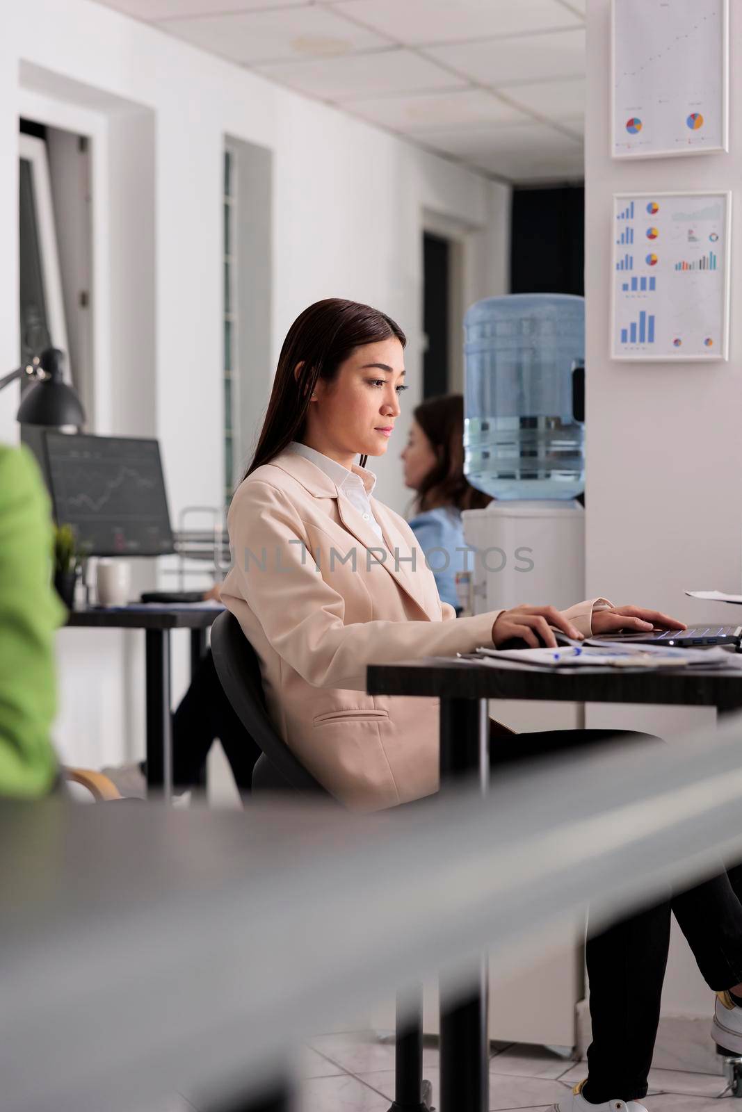 Young asian woman working on laptop in business office, company manager sitting at workplace desktop. Serious employee in modern coworking space, confident worker side view