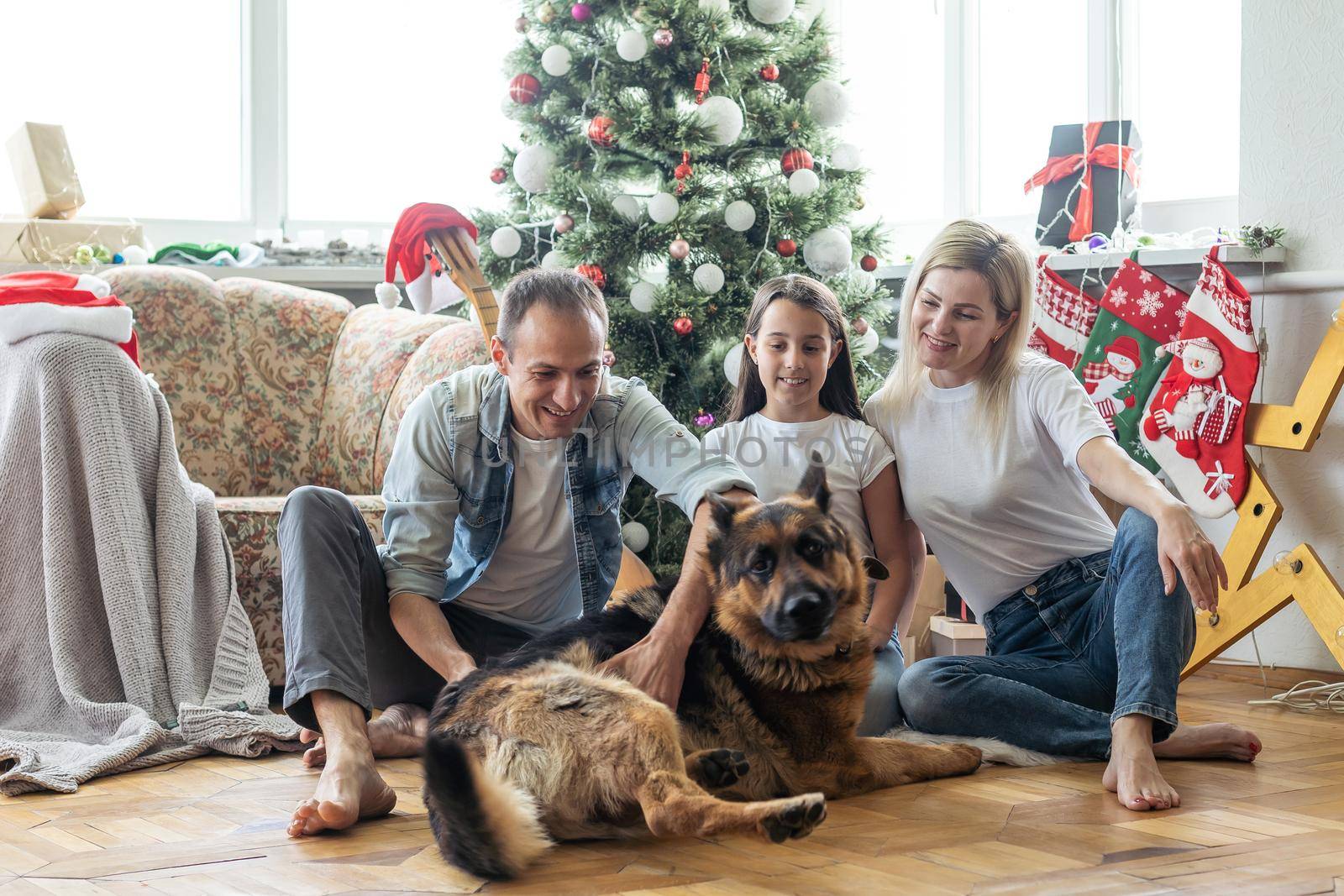 smiling family and daughter with dog sitting near christmas tree with gifts.