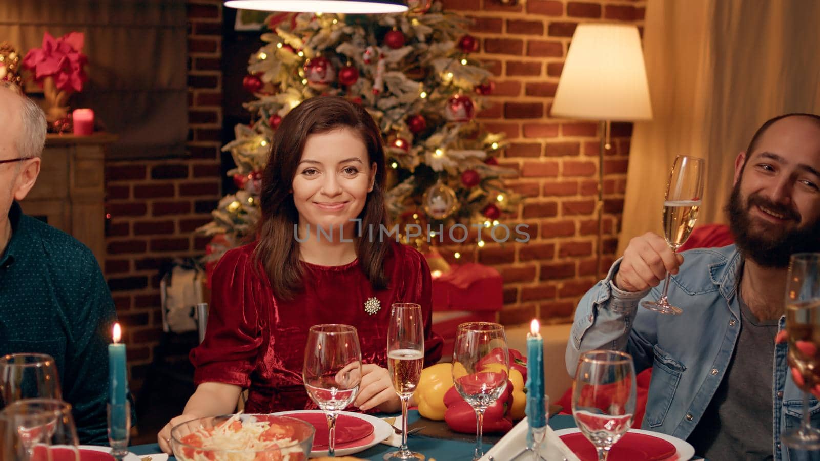 Gorgeous woman smiling heartily at camera while enjoying winter holidays with close family members. Festive wife talking with husband while celebrating Christmas at evening dinner family table.