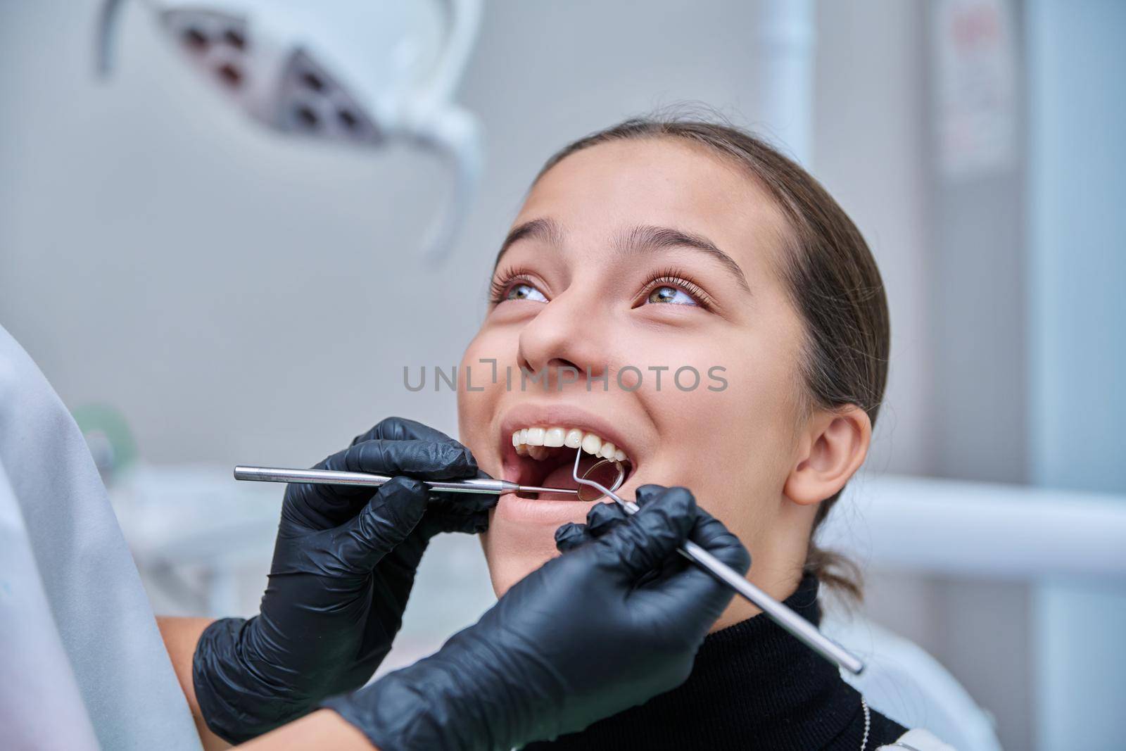 Young teenage female at dental checkup in clinic. Teenage girl sitting in chair, doctor dentist with tools examining patient's teeth. Adolescence, hygiene, dentistry, treatment, dental health care