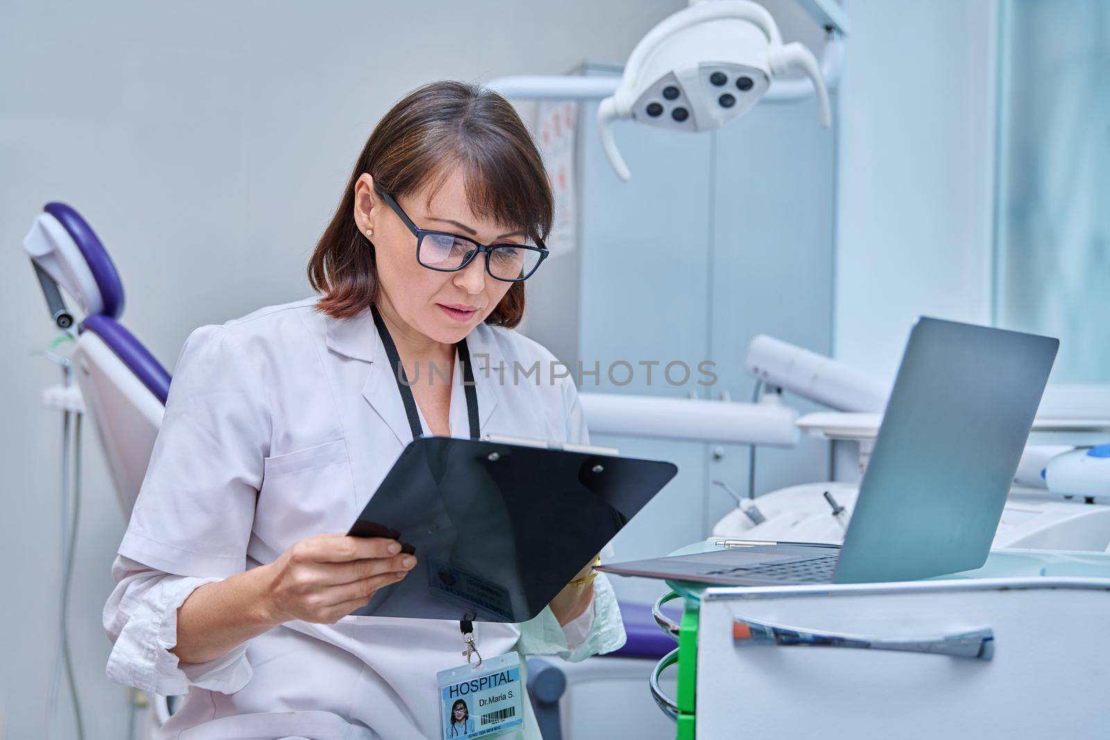 Doctor dentist working in office, using laptop, making notes on clipboard by VH-studio
