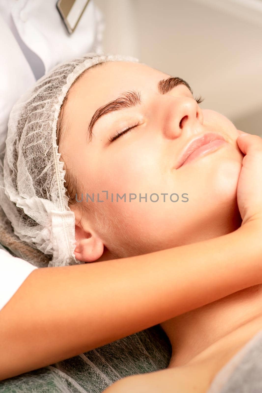 Facial massage. Hands of a masseur massaging neck of a young caucasian woman in a spa salon, the concept of health massage. by okskukuruza