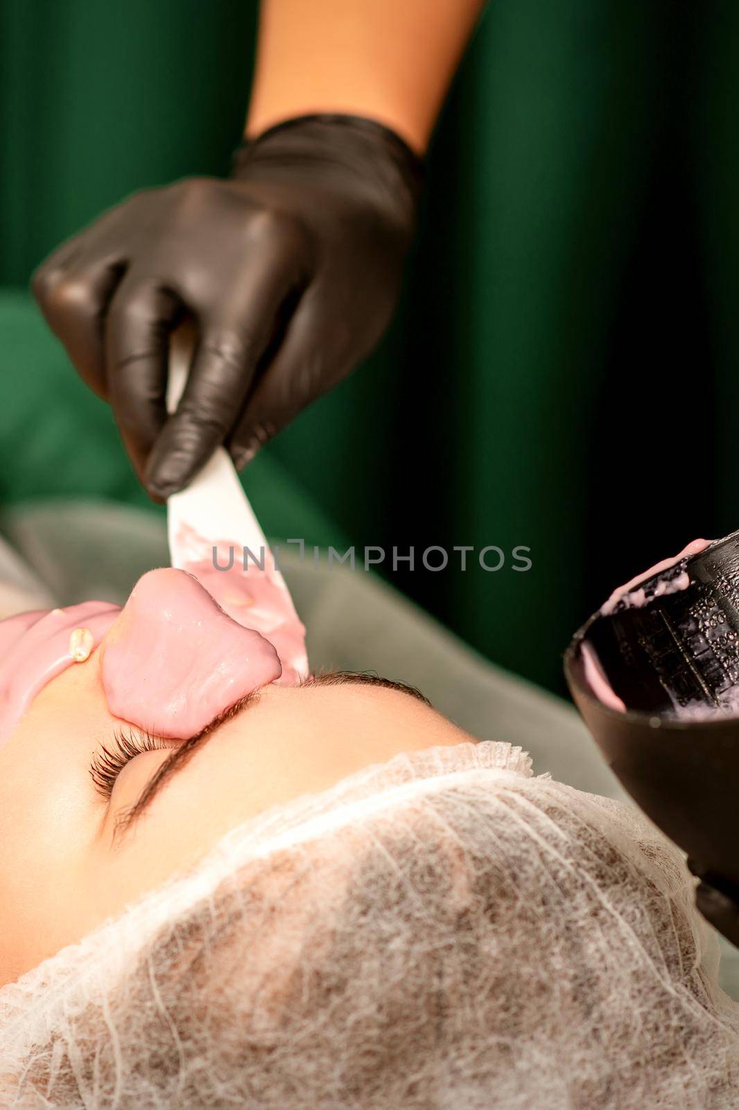 Beautiful young caucasian woman receiving an alginic mask to the face in beauty salon. Facial skin treatment. by okskukuruza