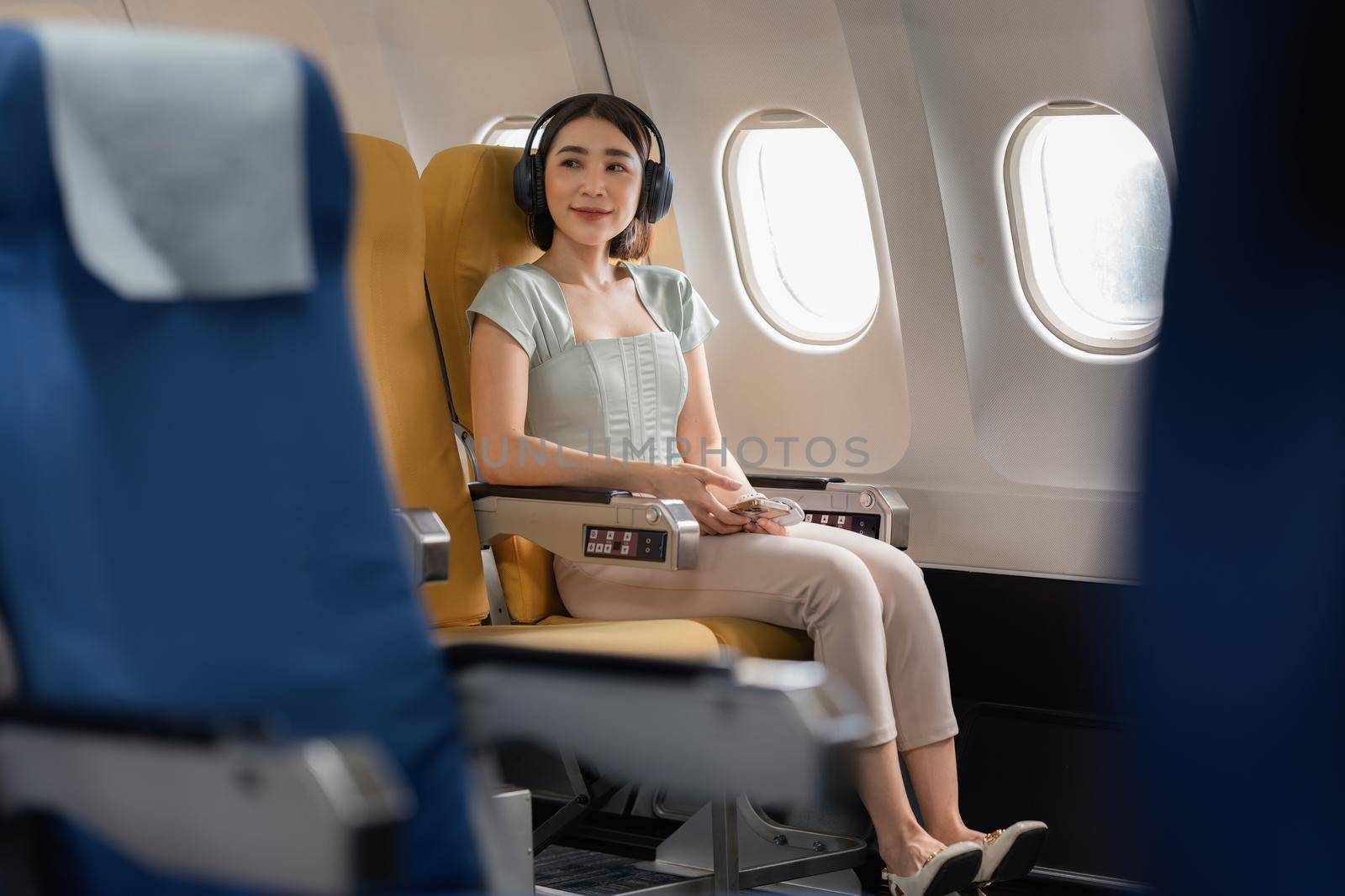 Joyful asian woman sits in the airplane and listen music while go to travel.