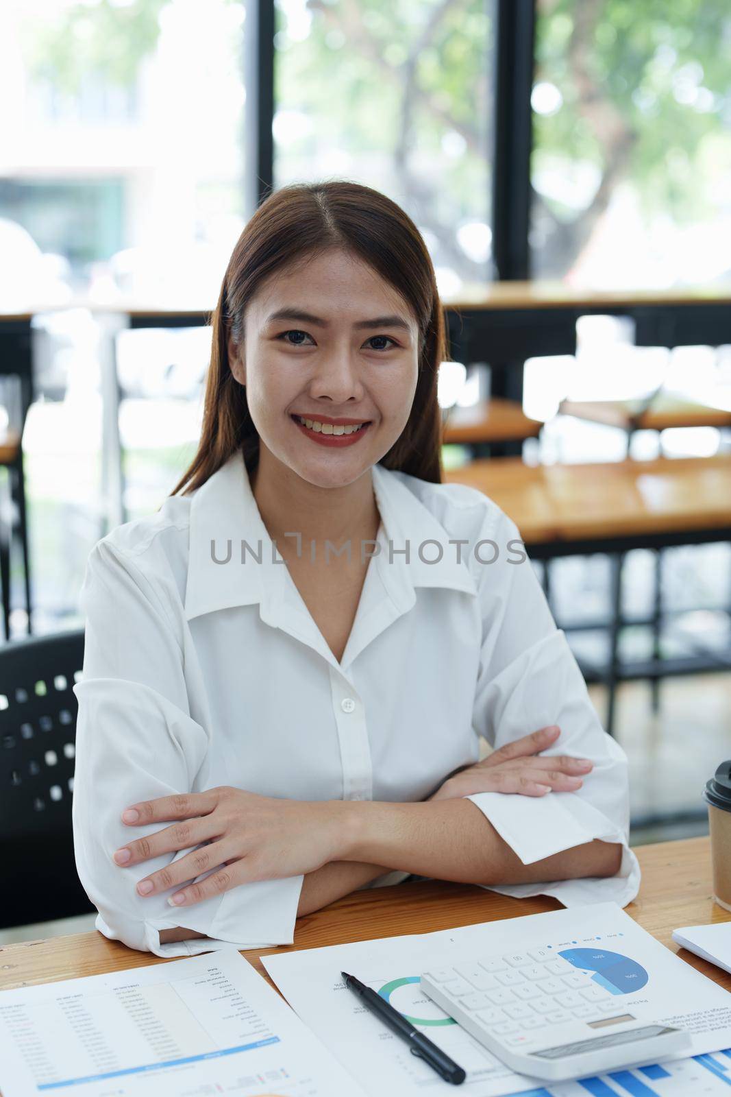 Portrait of a female business owner showing a happy smiling face as he has successfully invested his business using computers and financial budget documents at work.