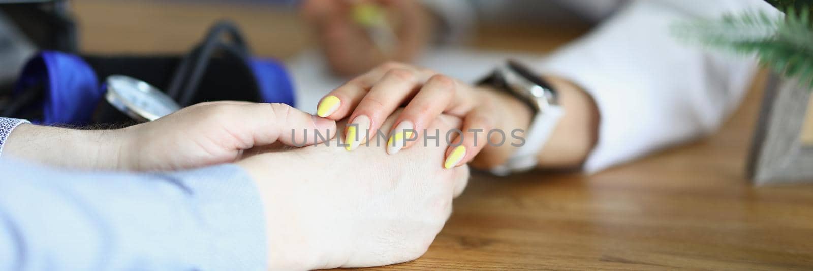 Woman doctor calms the patient, hands on the table close-up by kuprevich