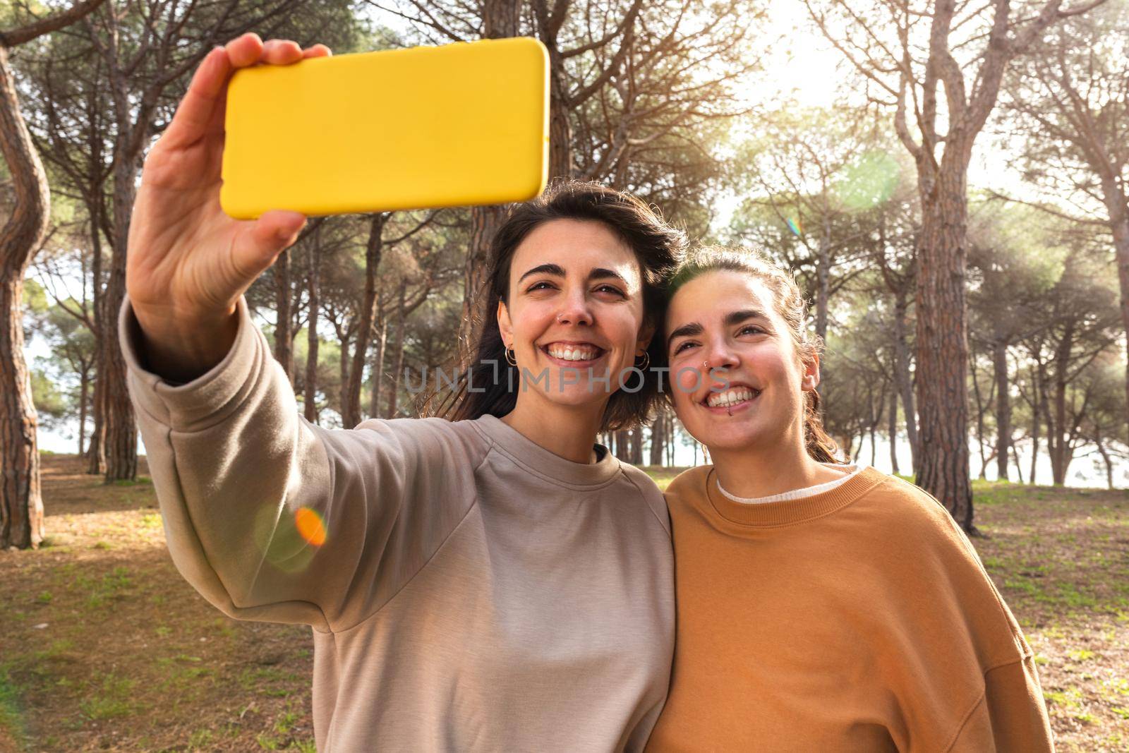 Happy and smiling young caucasian women take selfie using mobile phone in the forest. Hiking and nature concepts.