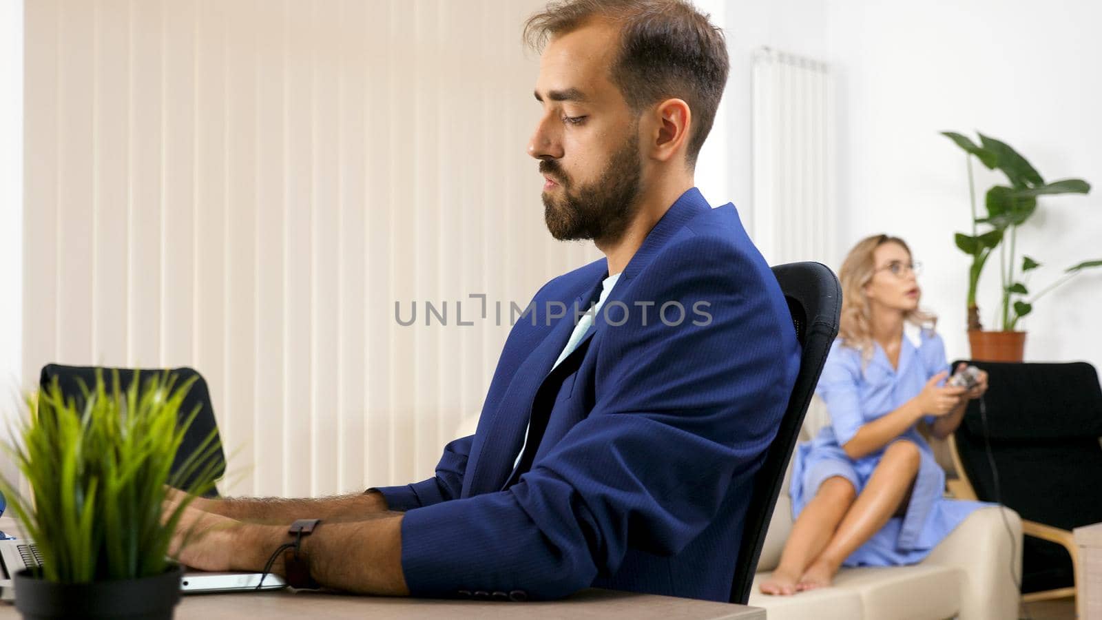 Freelancer businessman working on the laptop computer in the house and his wife is in the background