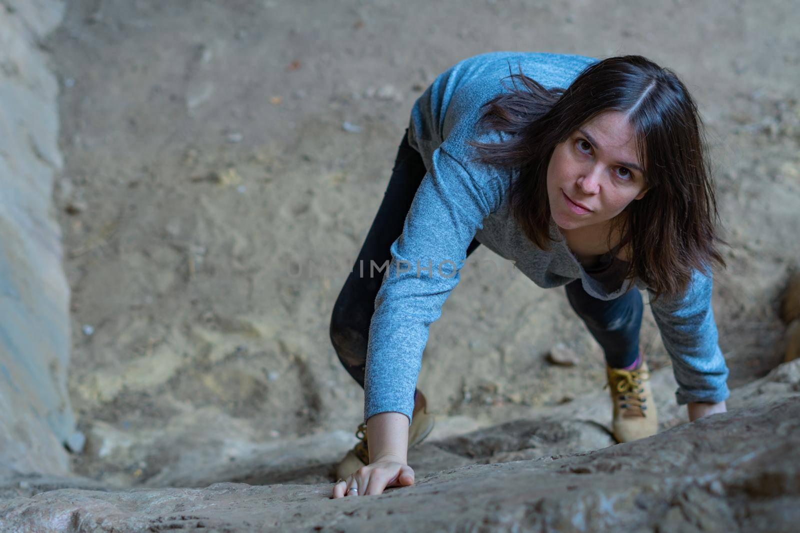 young girl learning rock climbing in high mountain with blue sweater, black tights and boots.