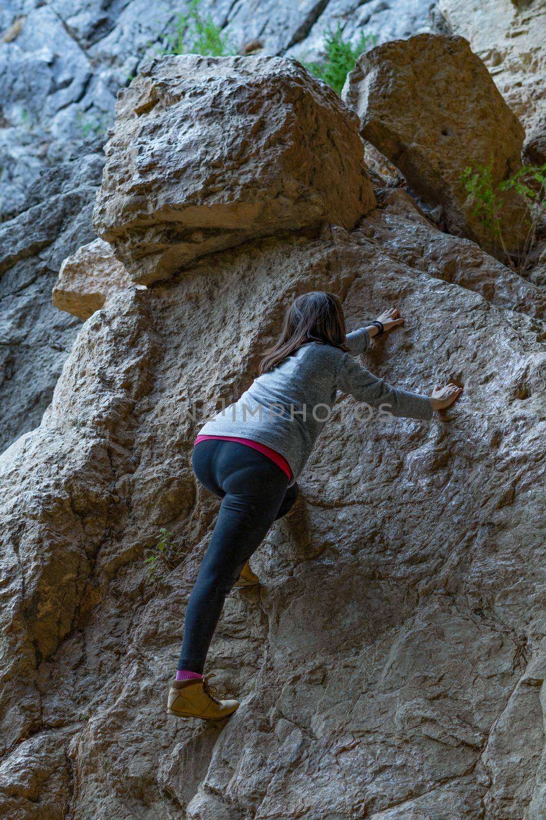 young girl learning rock climbing in high mountain with blue sweater, black tights and boots.