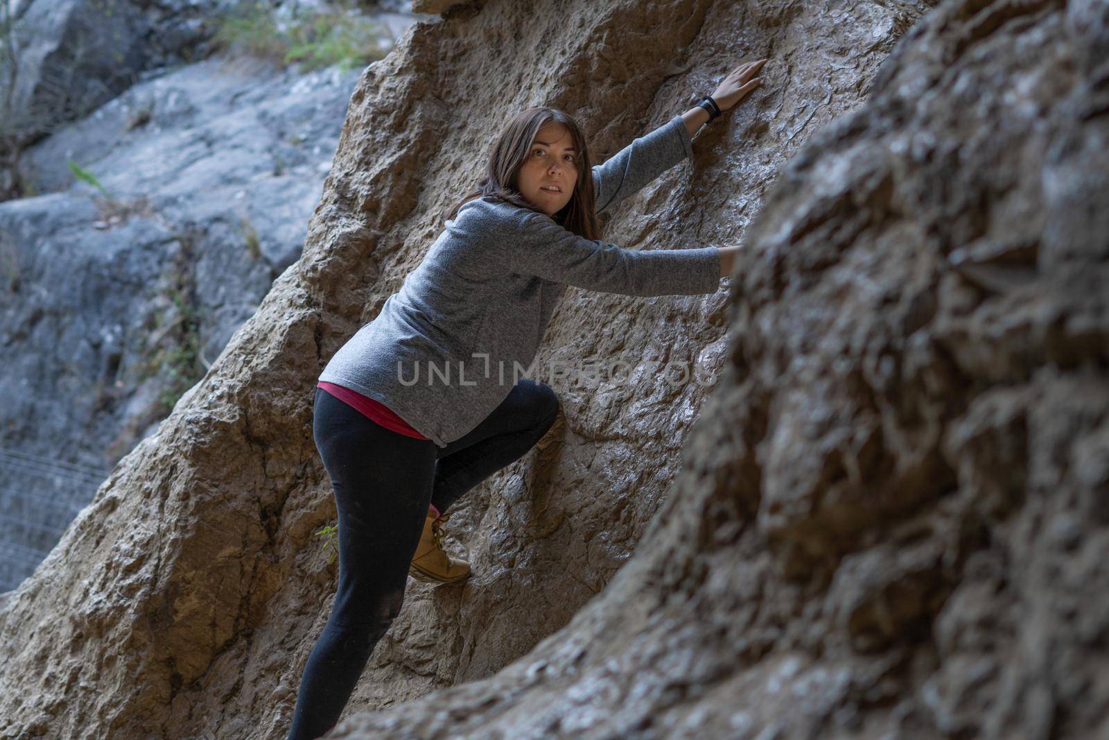 young girl learning rock climbing in high mountain with blue sweater, black tights and boots.