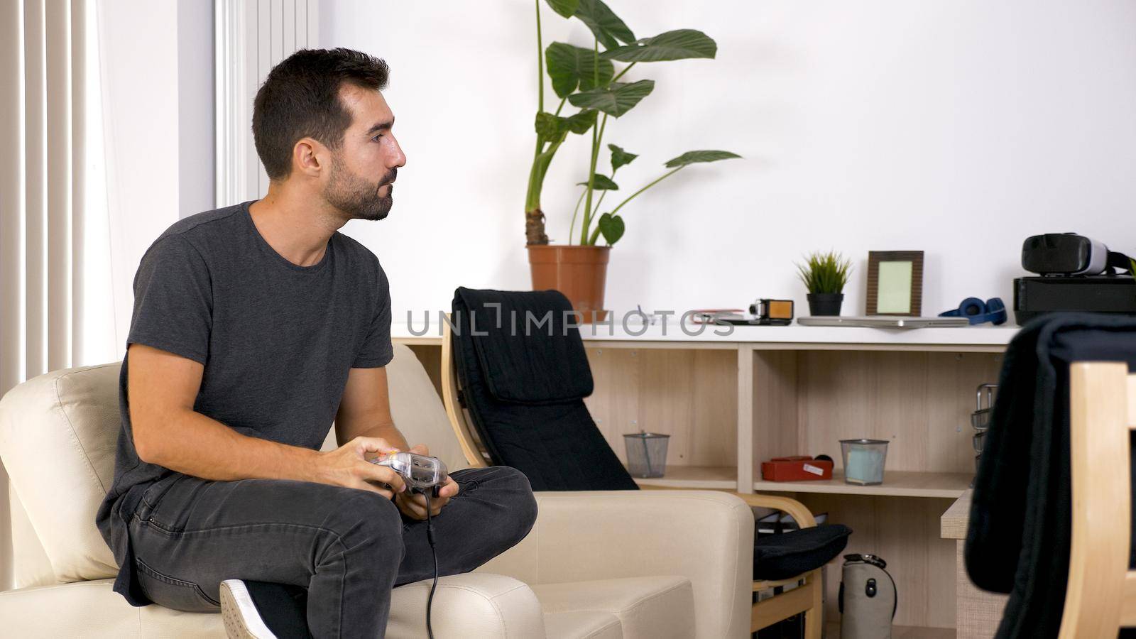 Attractive young man sitting on his couch and playing video games. Relaxing being home.