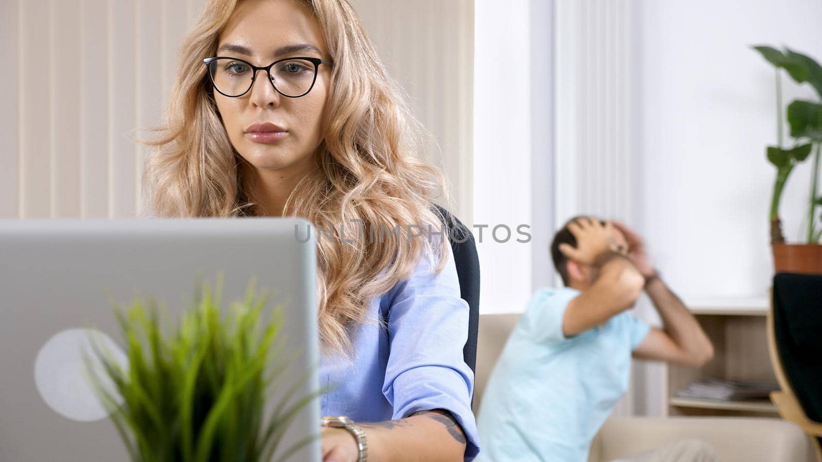 Freelancer woman working on the computer laptop in the house while the husband is watching TV in the background