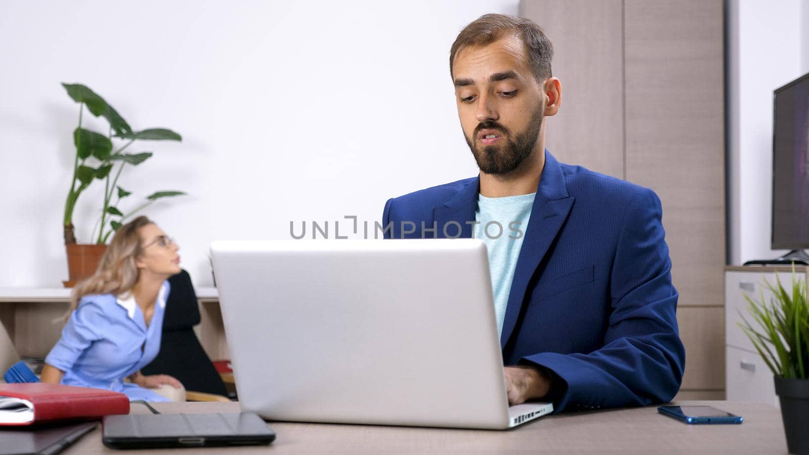 Freelancer businessman working on the laptop computer in the house and his wife is in the background