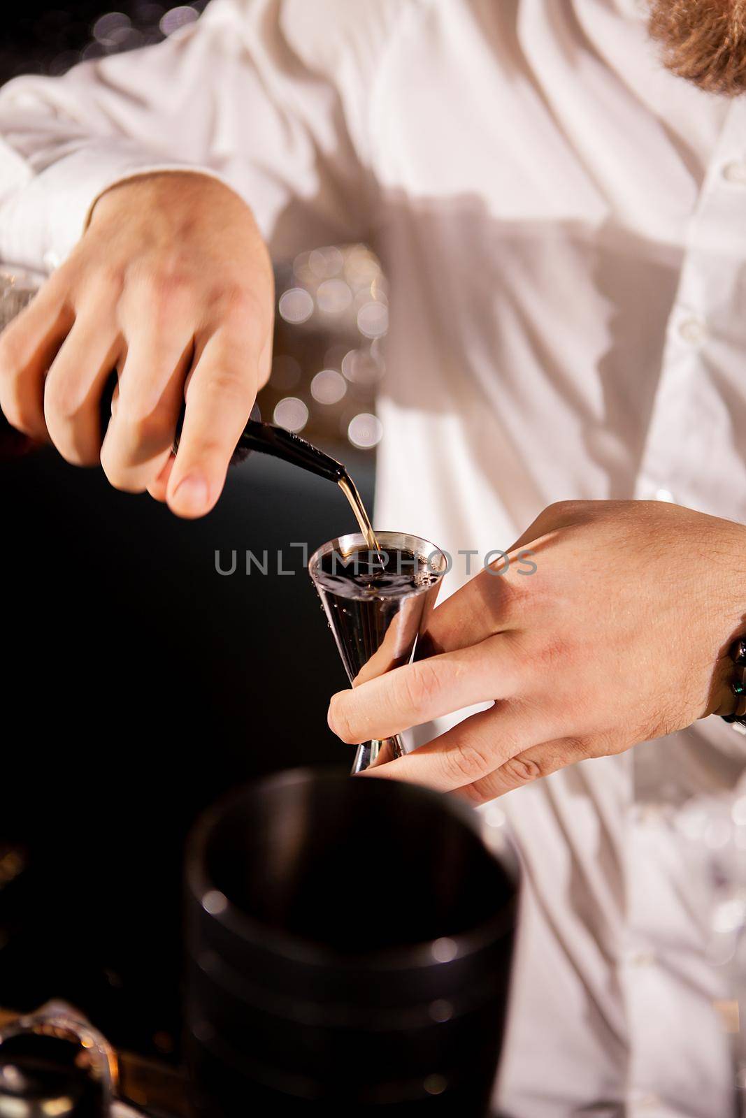 Barman adding cocktail ingredients.Barman in bar interior making alcohol cocktail.