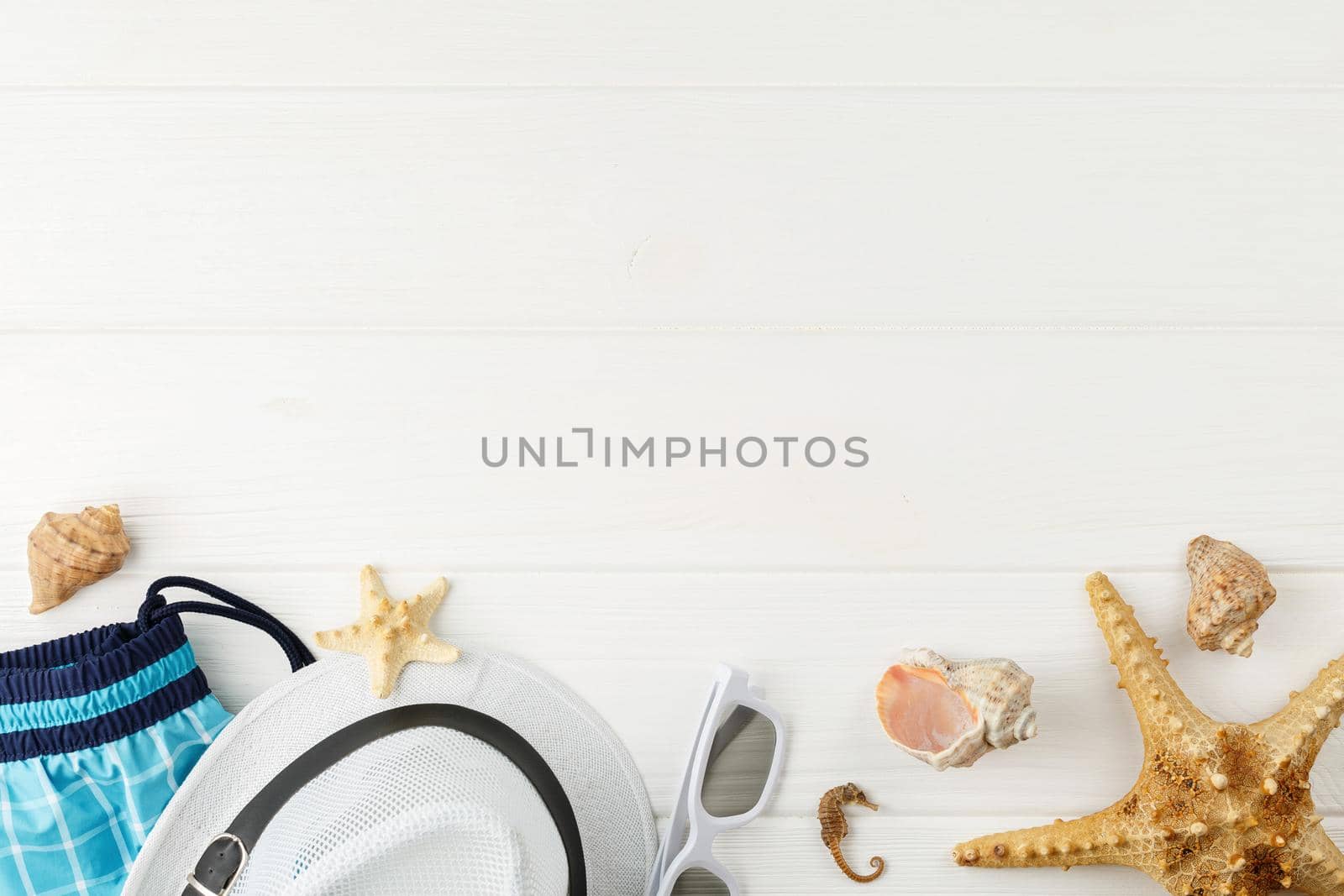 Beach hat with sunglasses and shorts on white wooden background Copy space. Flat lay. Summer vacation concept. Starfish and seashells. Top view.