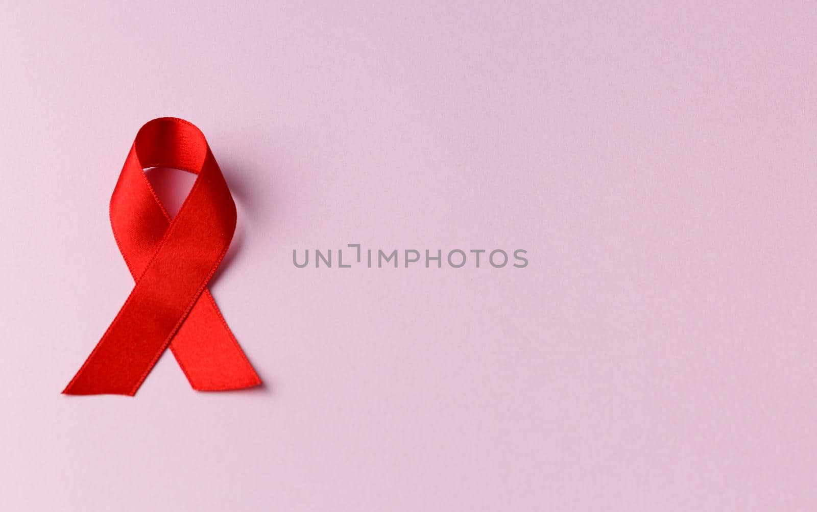 Red ribbon on a pink background. Top view. Health care. AIDS prevention concept. Hiv and cancer awareness. Flat lay.