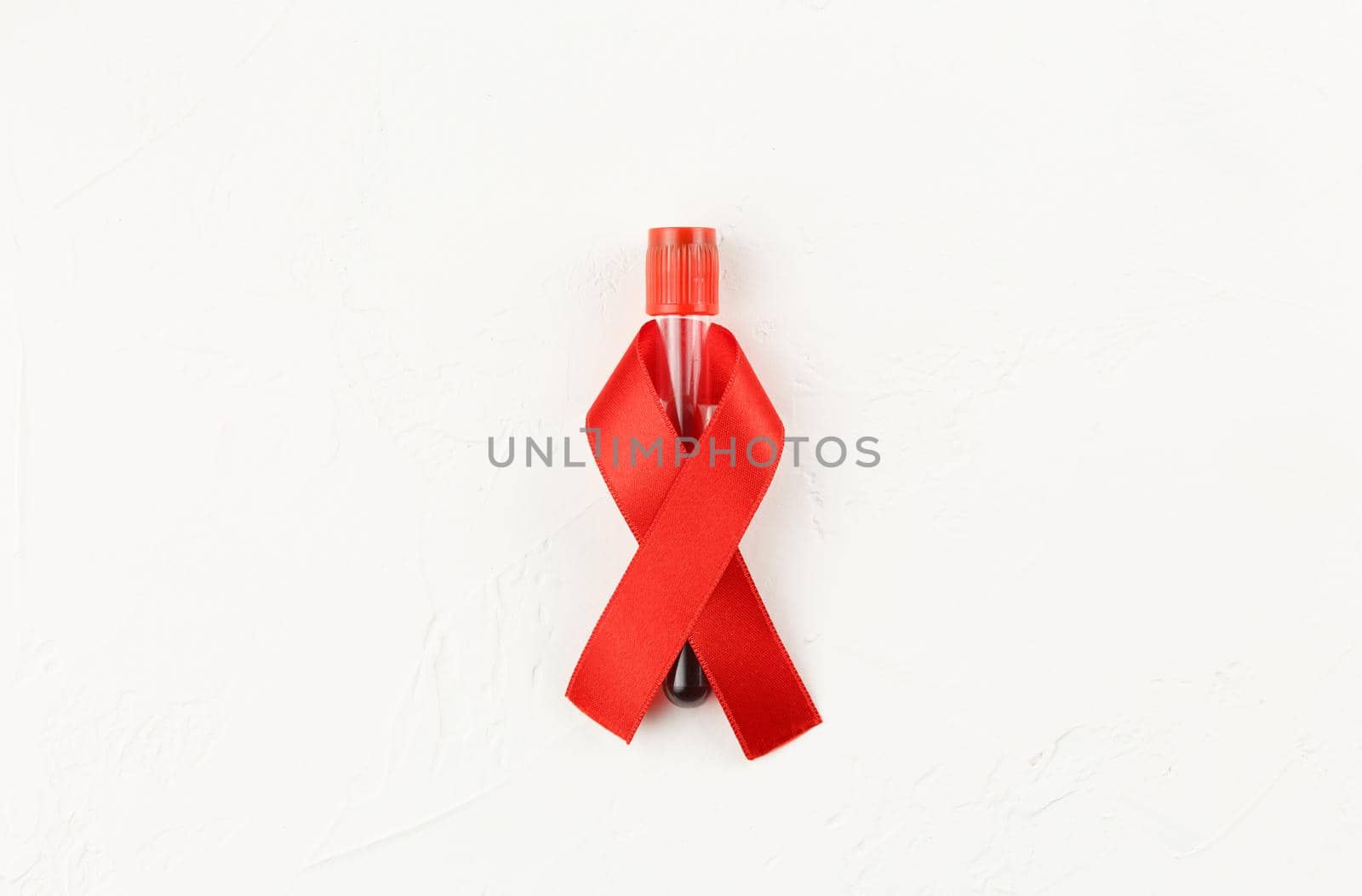 Red ribbon with vacutainer on a white grunge background. Top view. Health care. AIDS prevention concept. Hiv and cancer awareness. Test tube container. Flat lay.