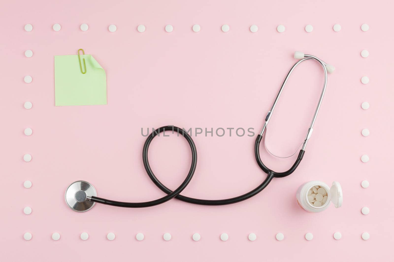 Stethoscope with a sticker in a frame of pills on a pink background. Top view.