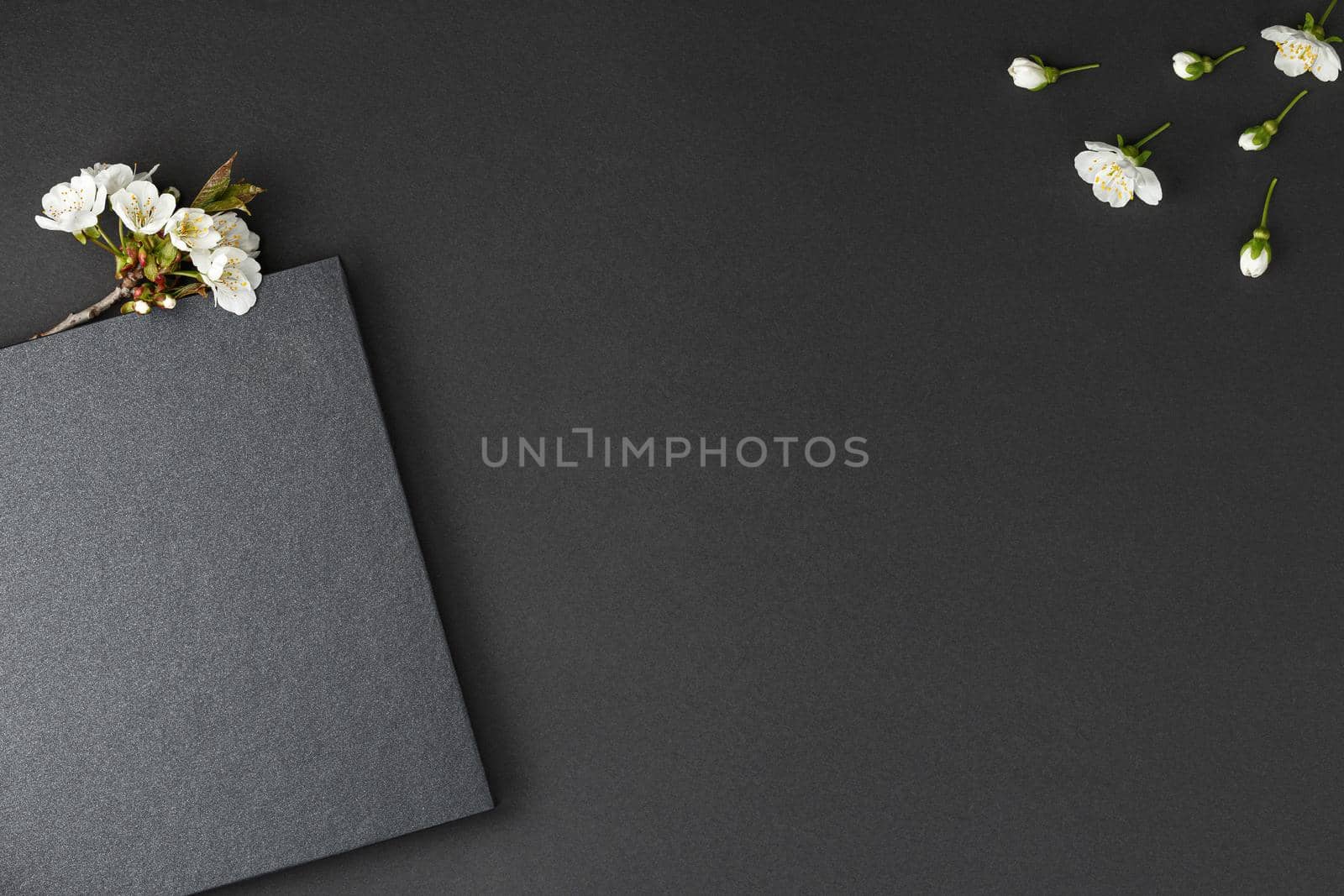 Black notebook with white cherry flowers on dark isolated background flat lay.