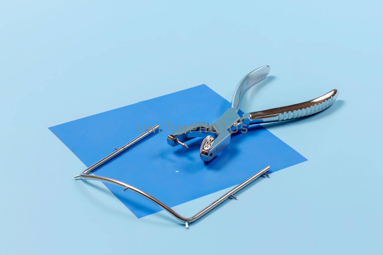 Dental hole punch, metal frame and rubber dam on blue. by mvg6894