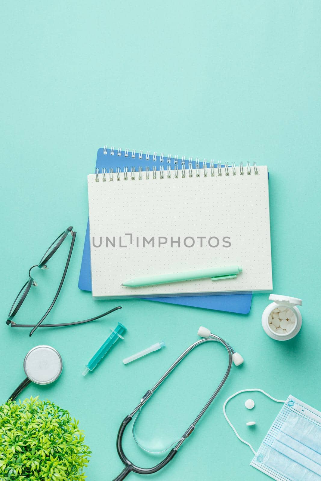 Medical equipment with stethoscope and spiral notebook in doctor office on green desk background top view. Nurse desktop concept.