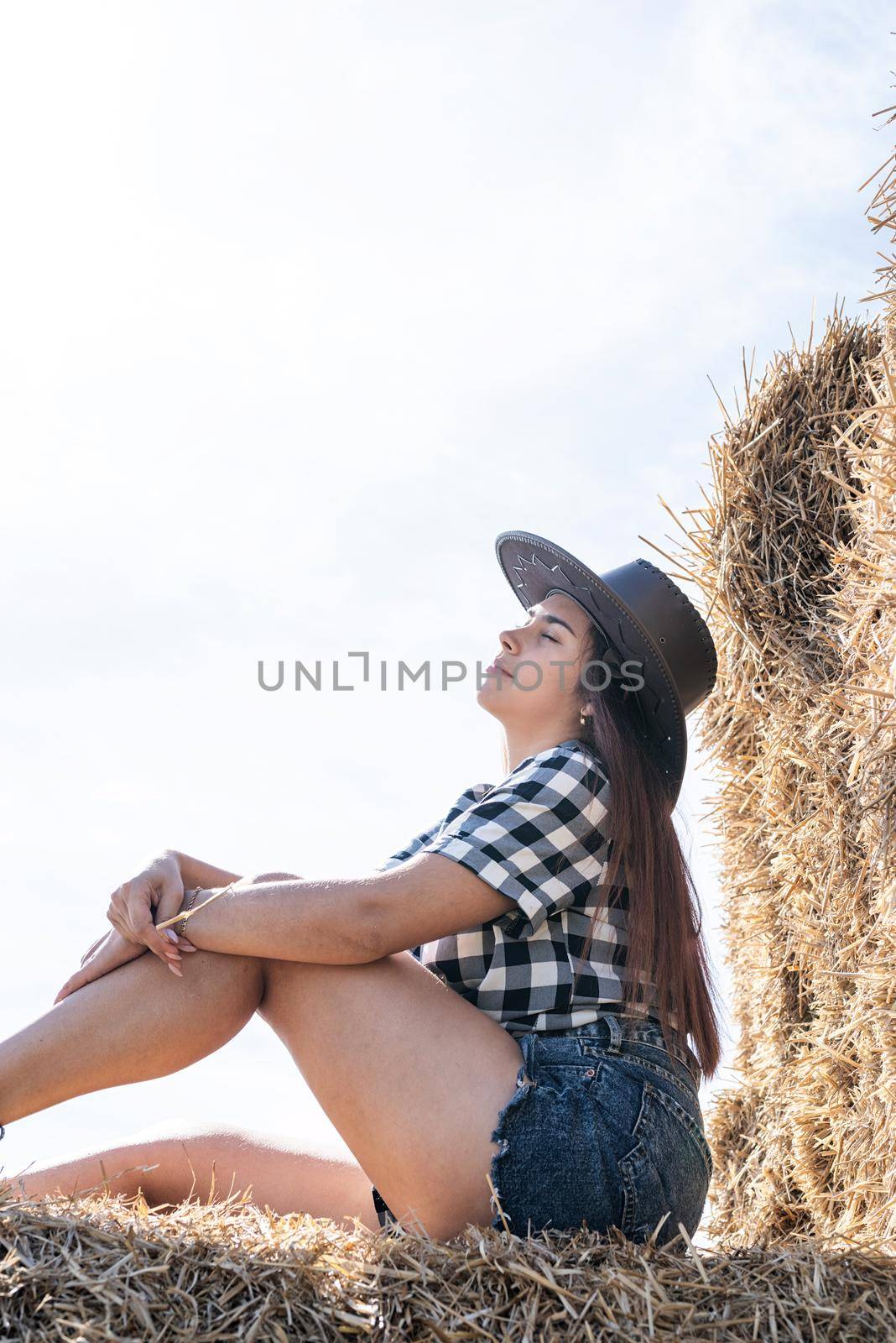 Beautiful girl on straw bales. beautiful woman in plaid shirt and cowboy hat resting on haystack