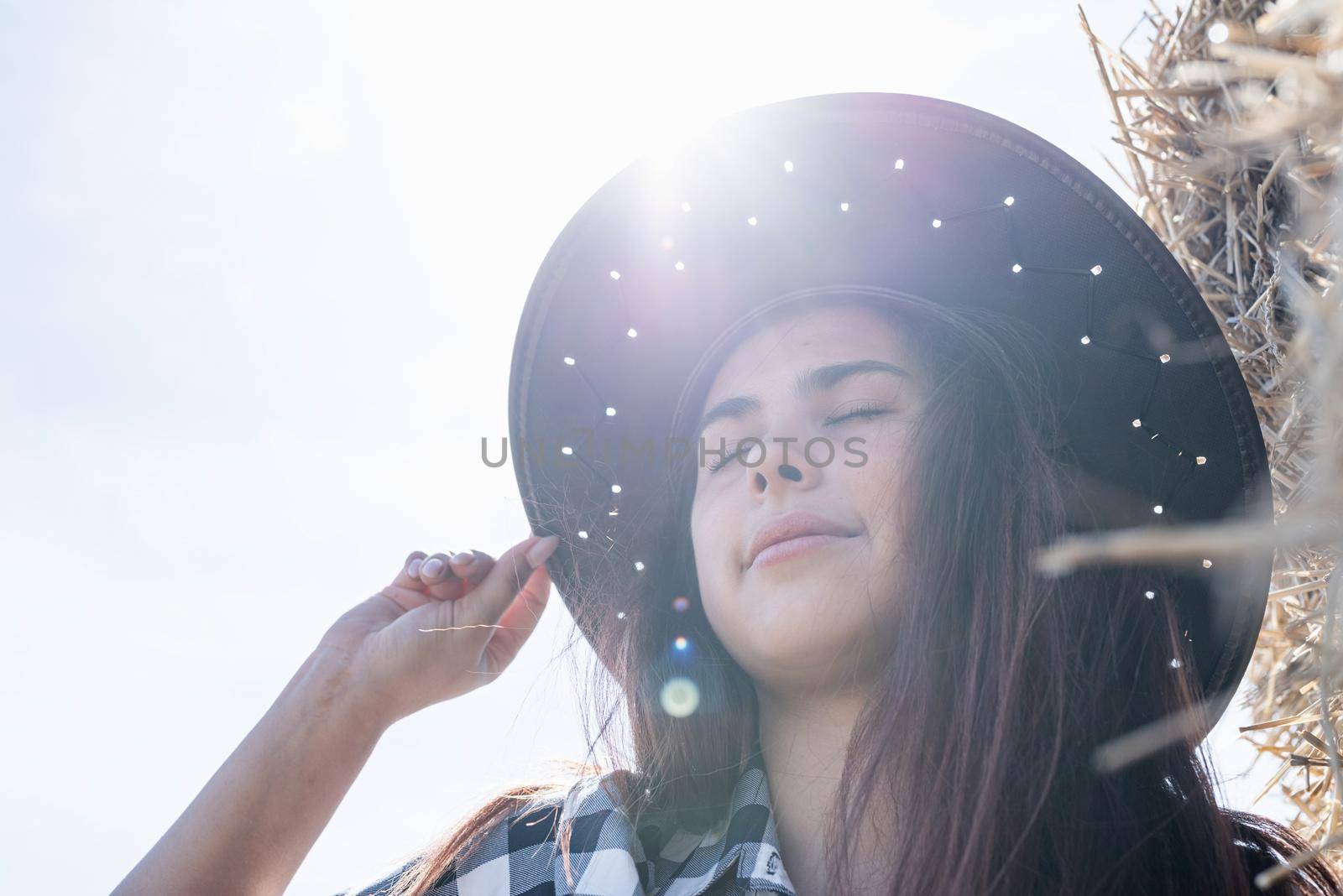 Beautiful girl on straw bales. beautiful woman in plaid shirt and cowboy hat resting on haystack