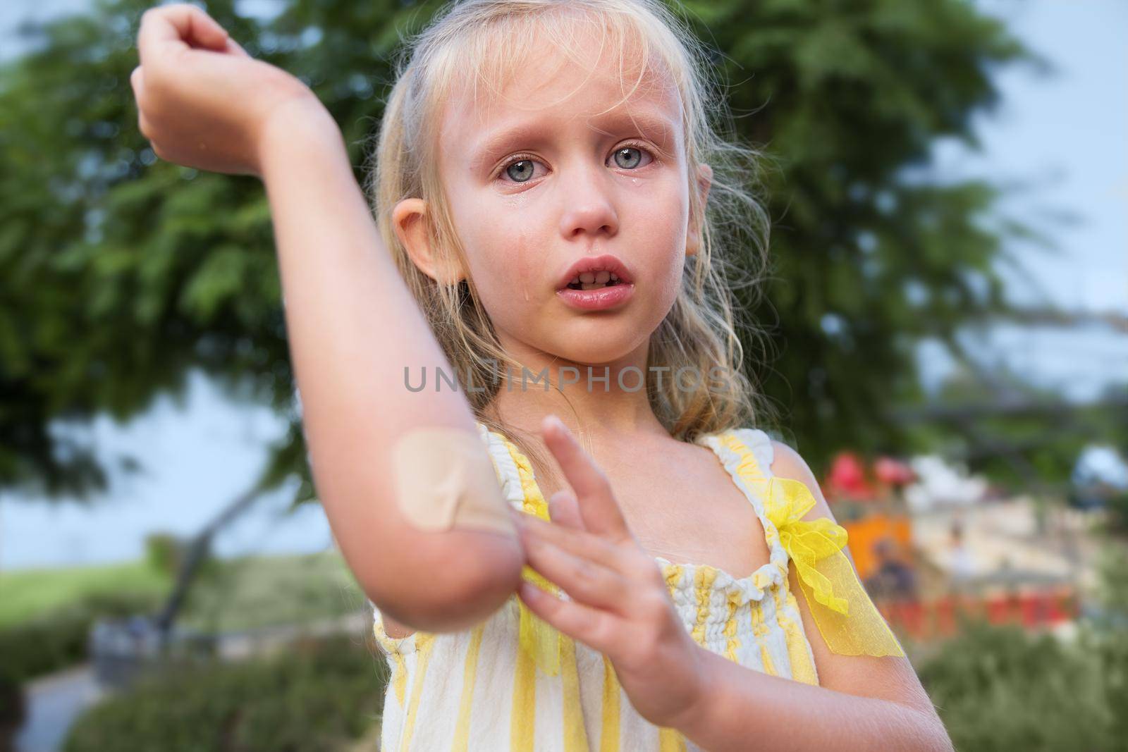 Close-up portrait of little girl. blonde, European appearance, summer day. the child fell in the park and injured his hand. Elbow injury, little girl crying. Tears on the face, pain, suffering, Summer