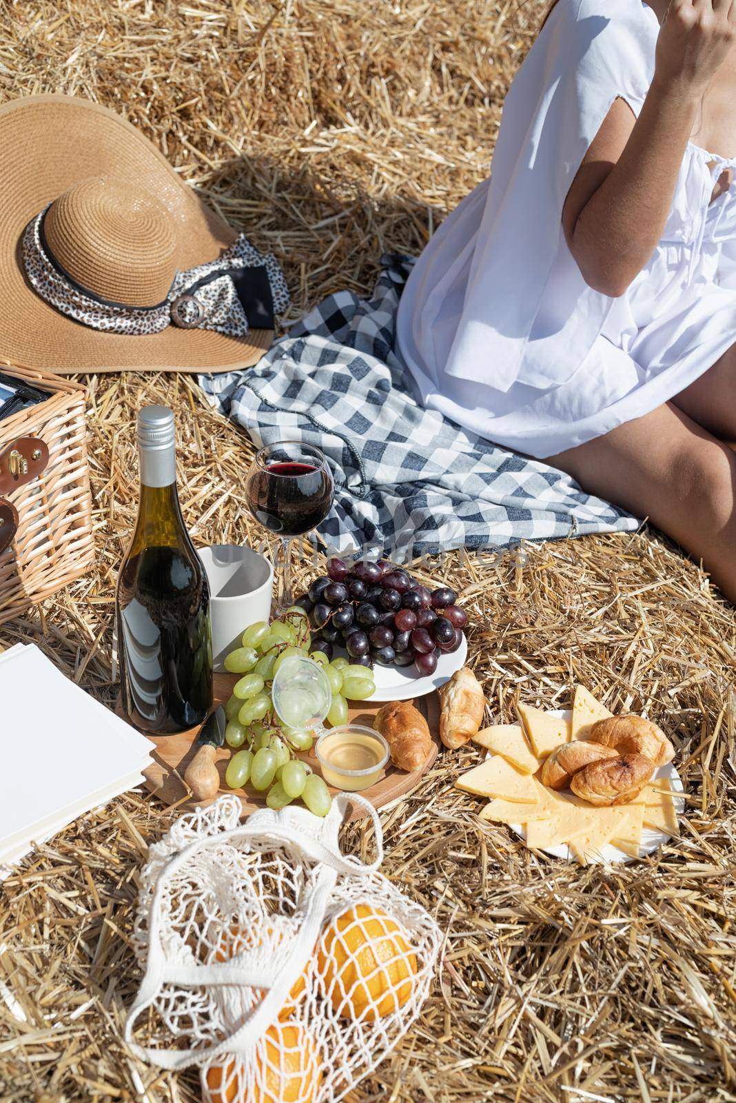 Young woman with wine glass sitting near haystack in harvested field by Desperada