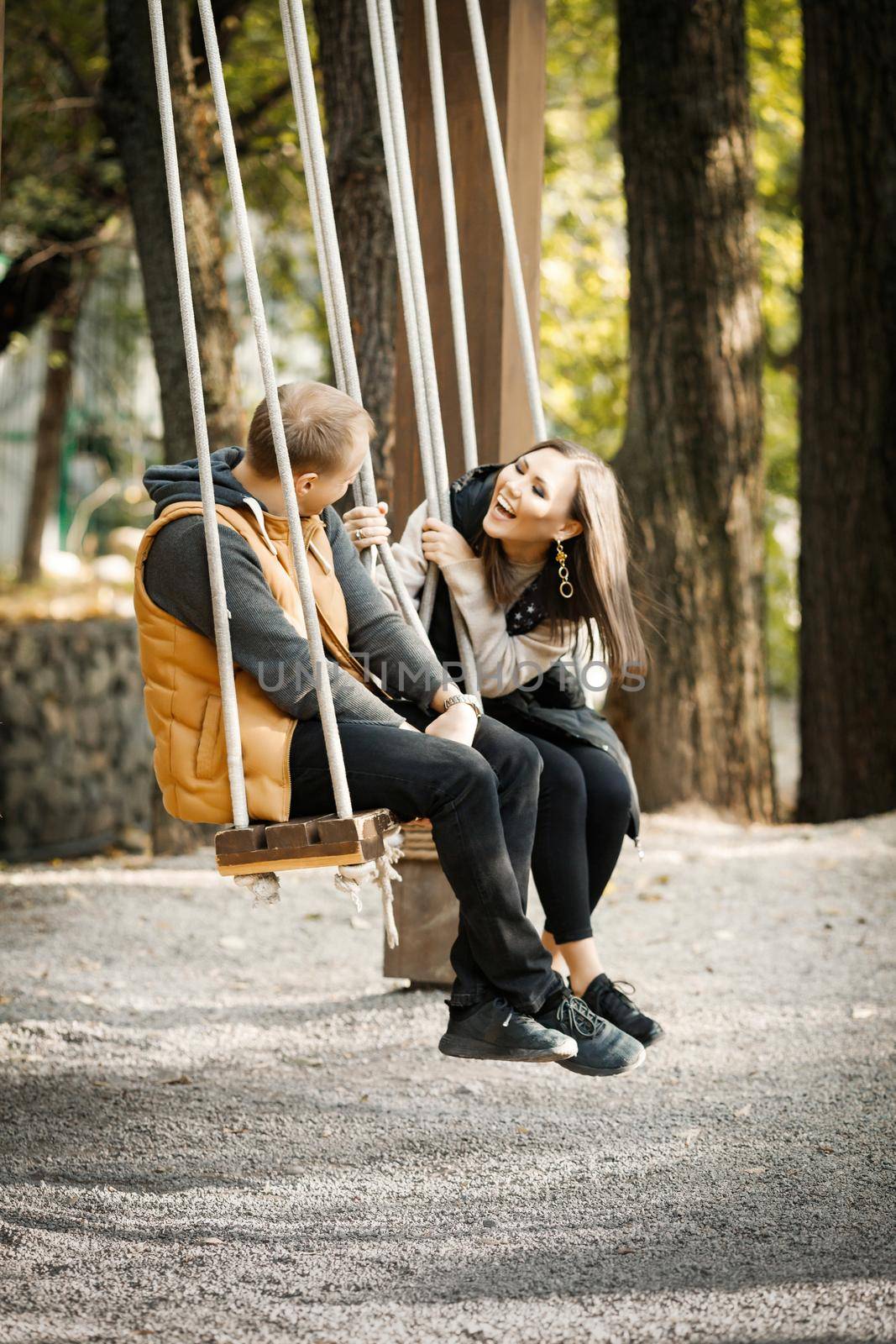 Vertical image of a happy couple in love on a swing in a forest park during the warm season by Rom4ek