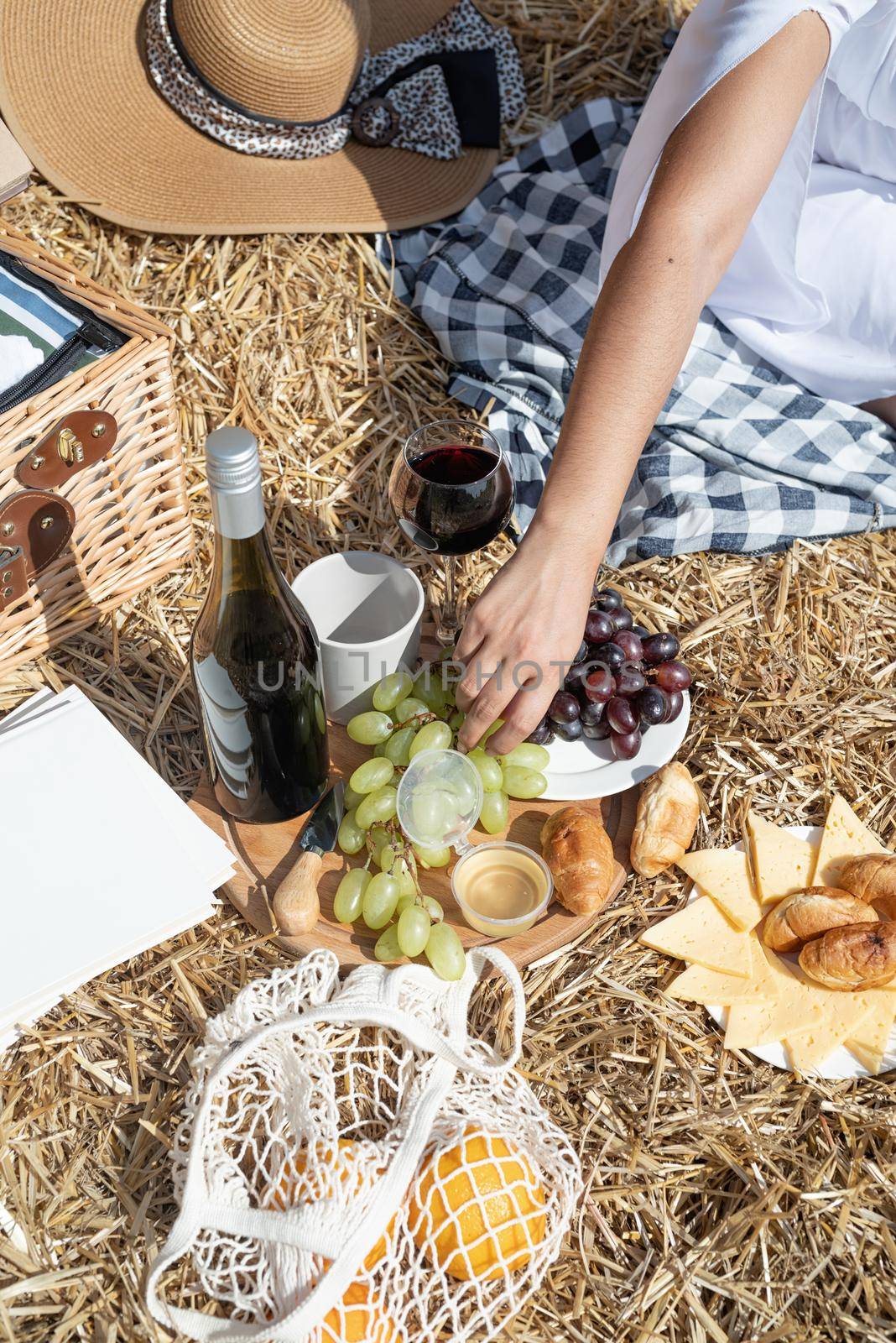 Young woman with wine glass sitting near haystack in harvested field by Desperada