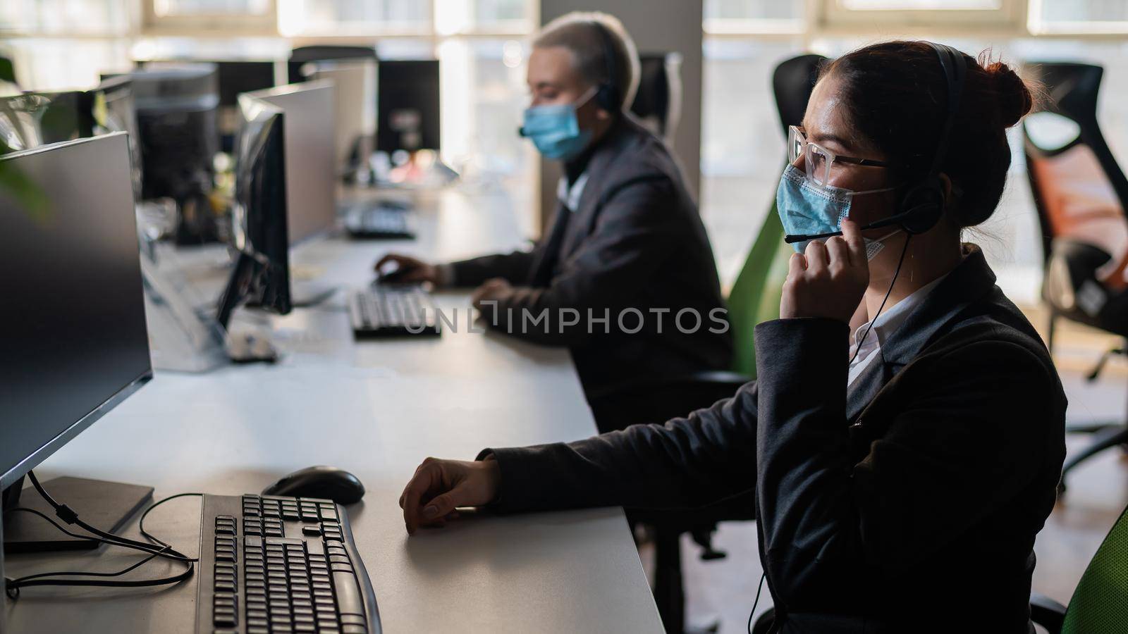 Two women in medical masks and headsets are working in the office.