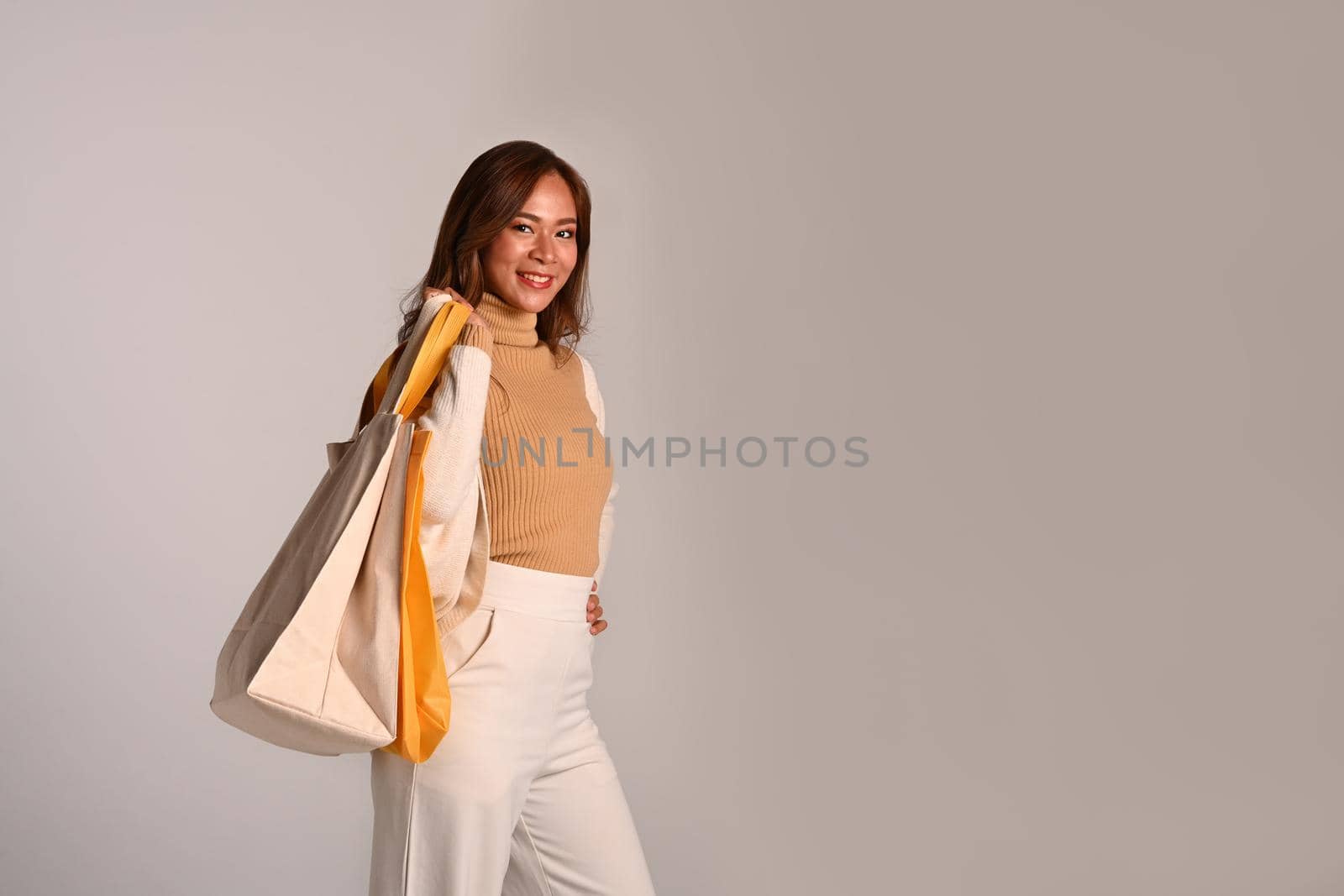 Portrait of beautiful woman carrying shopping bags standing on grey background. Black Friday, sale, shopping concept.