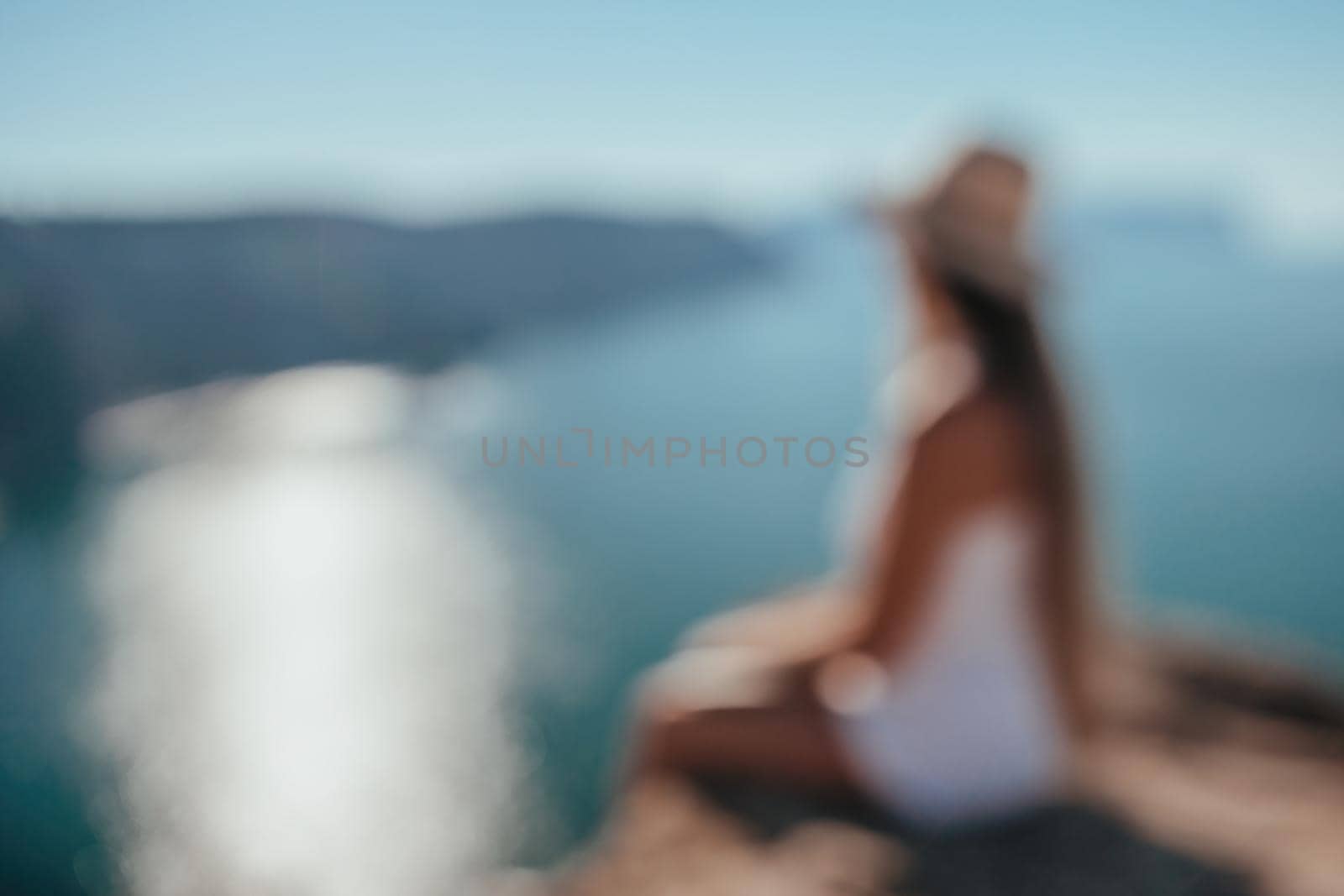 Abstract defocused digital nomad, woman in the hat, a business woman with a laptop sits on the rocks by the sea during sunset. Freelance, remote work on vacation. by panophotograph